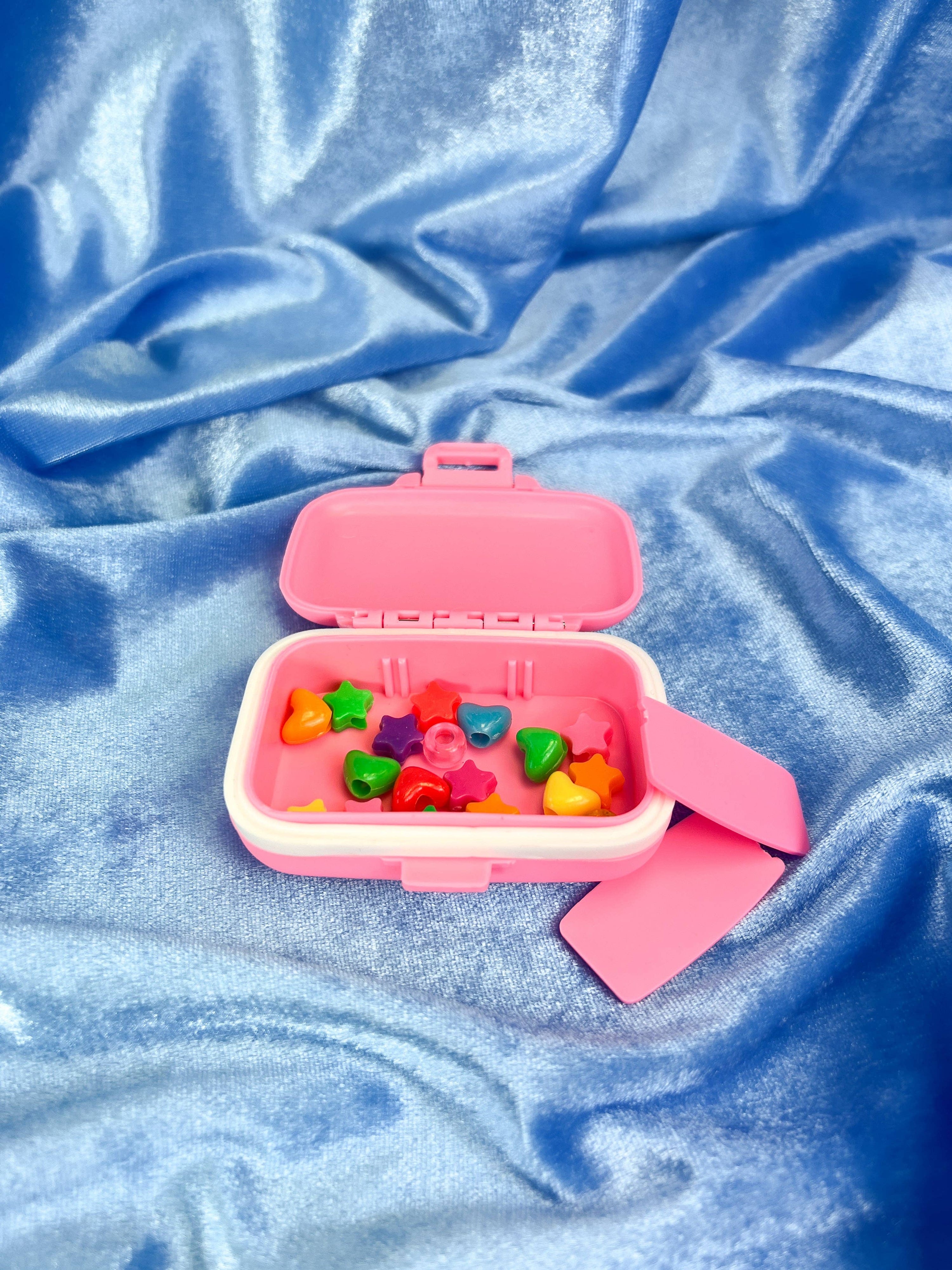 Pink pill box with colorful heart-shaped charms on a blue textured fabric background 