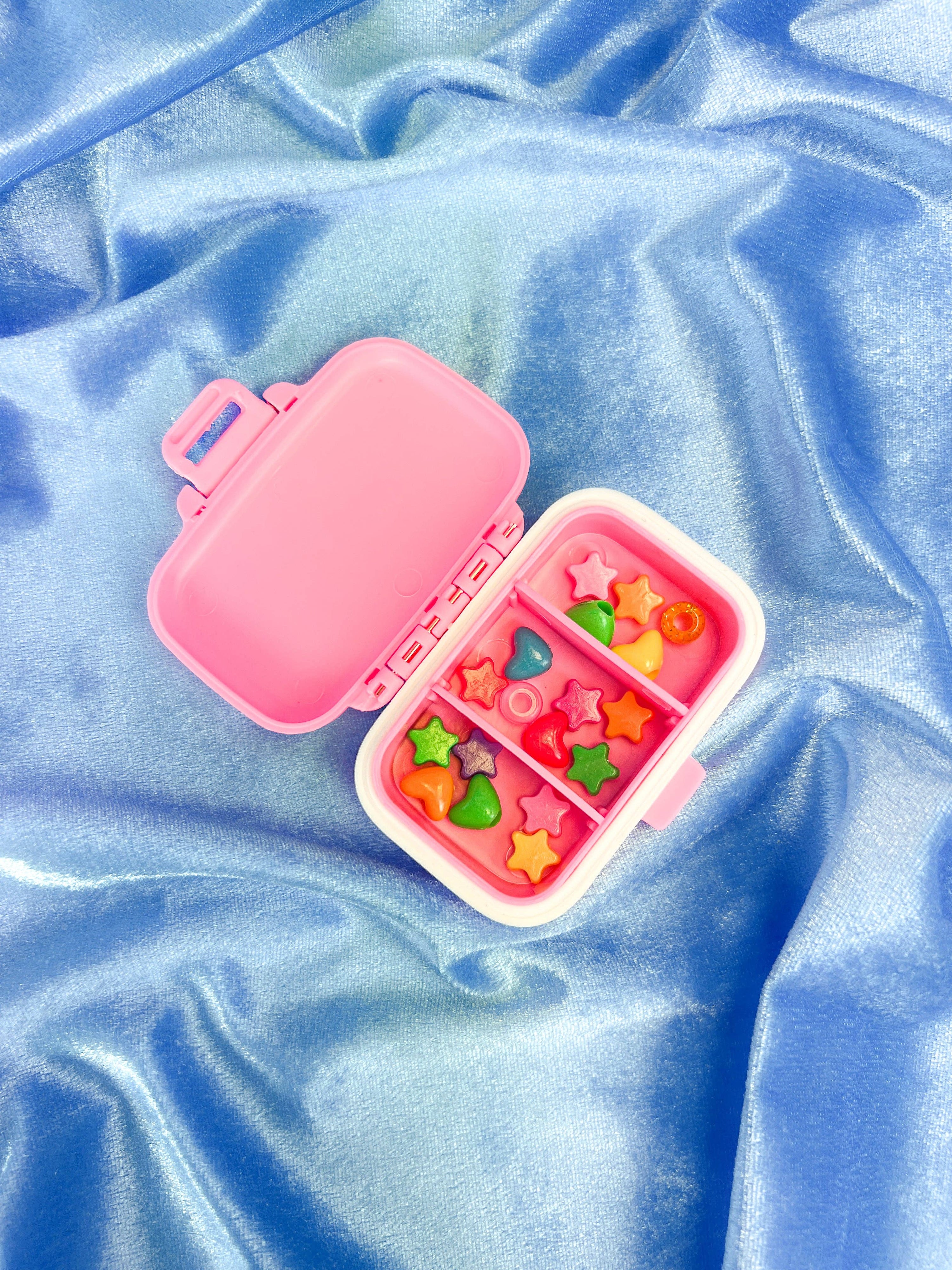 Pink pillbox with colorful compartments on a blue fabric background