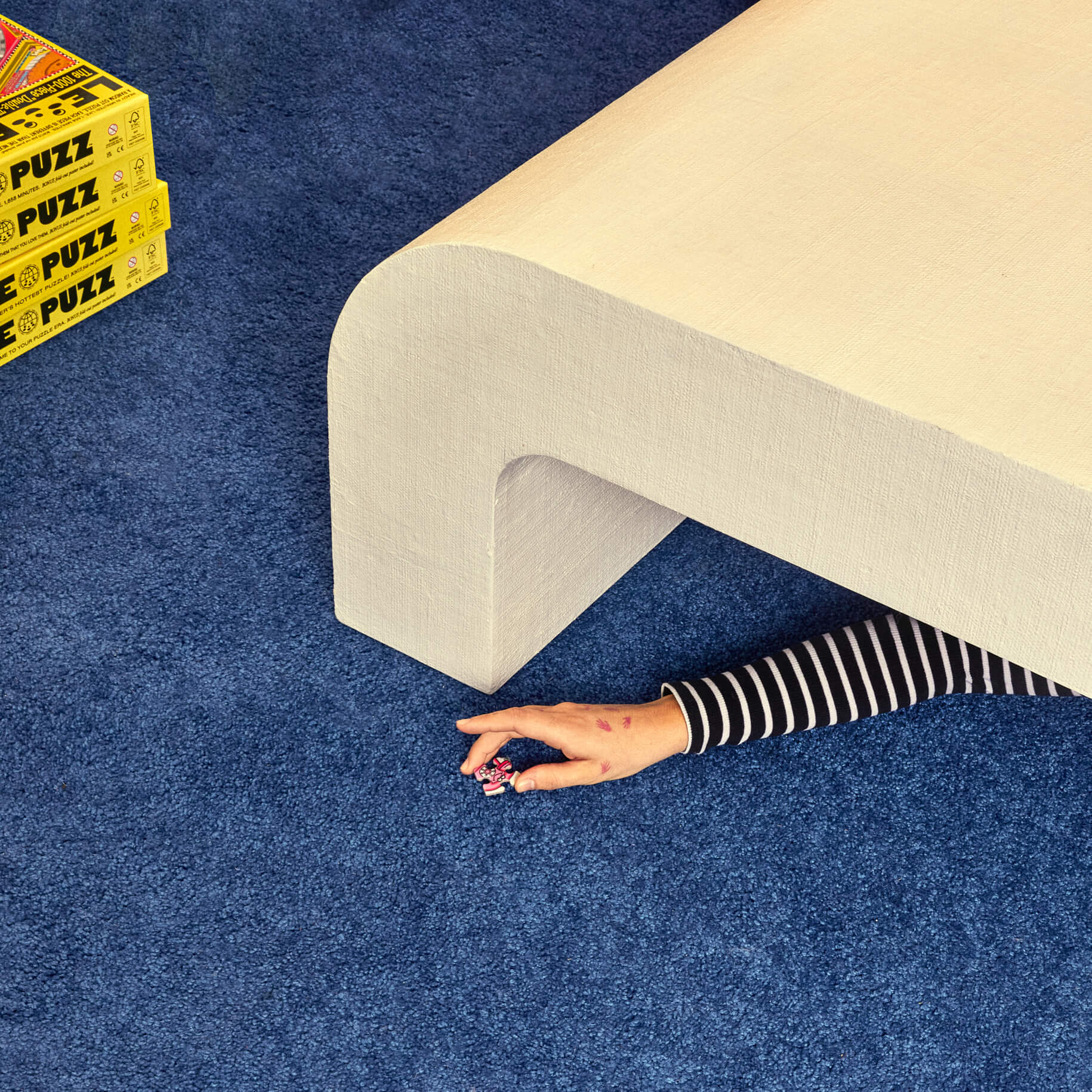Person rolling out a beige carpet on a blue floor with 'PUZZ' boxes nearby.