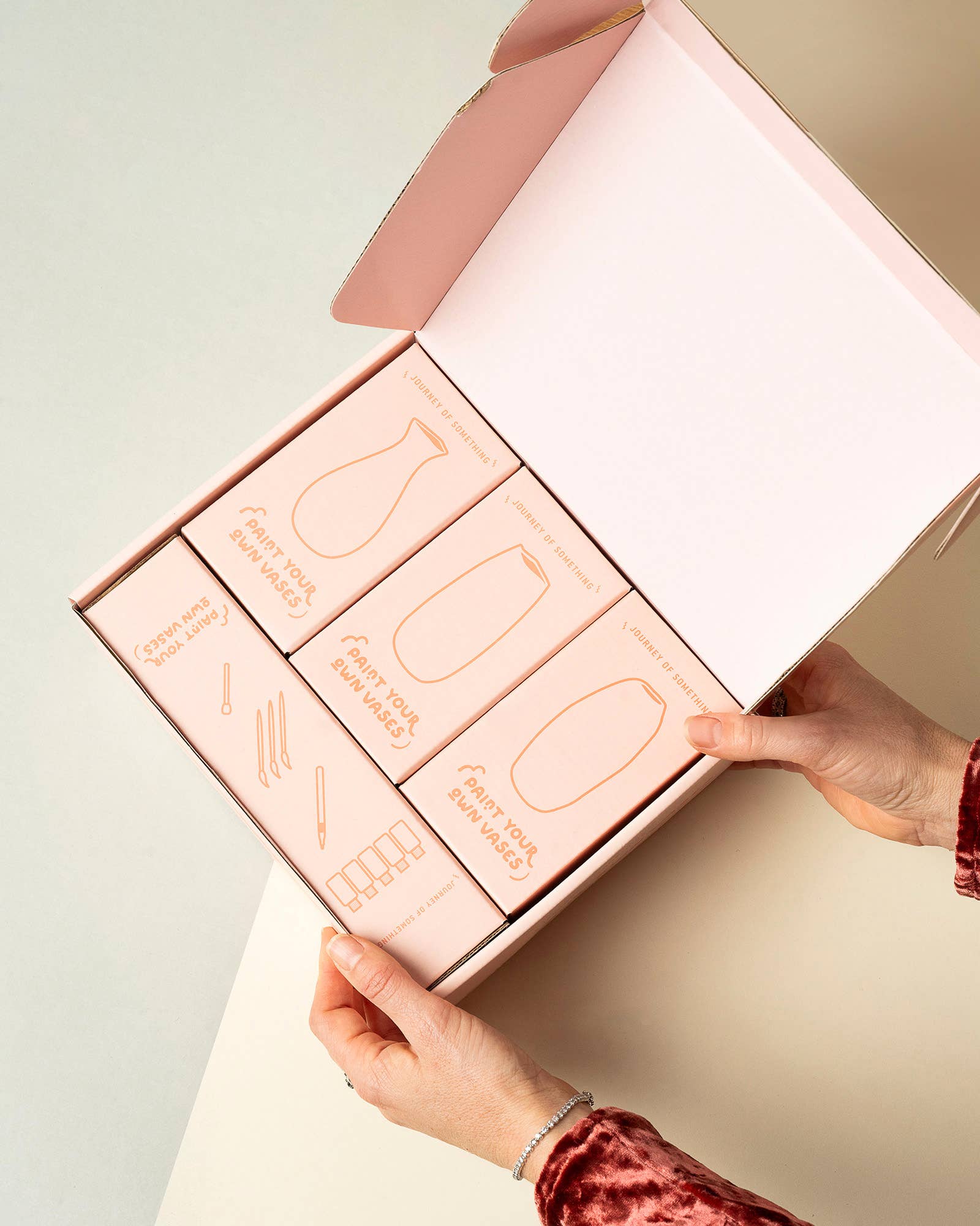 Pink skincare product set with a hand opening the box on a light background