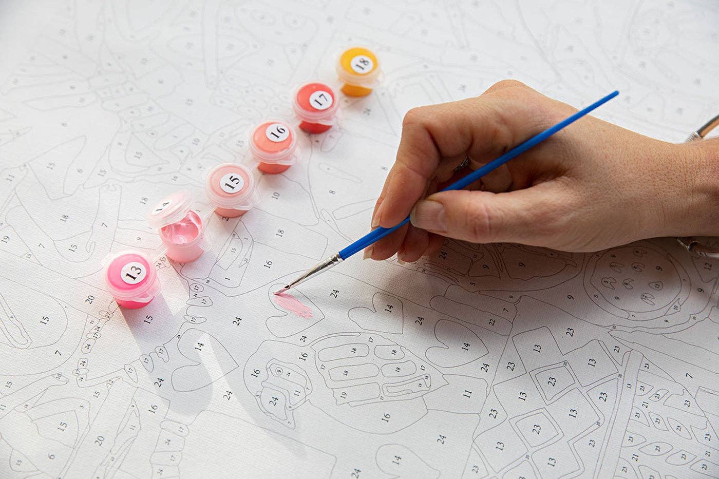 Hand holding a paintbrush with small containers of paint on a patterned surface