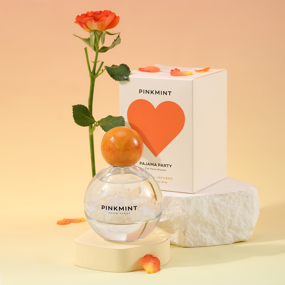 Pinkmint perfume bottle with orange cap, packaging, and rose on a beige background