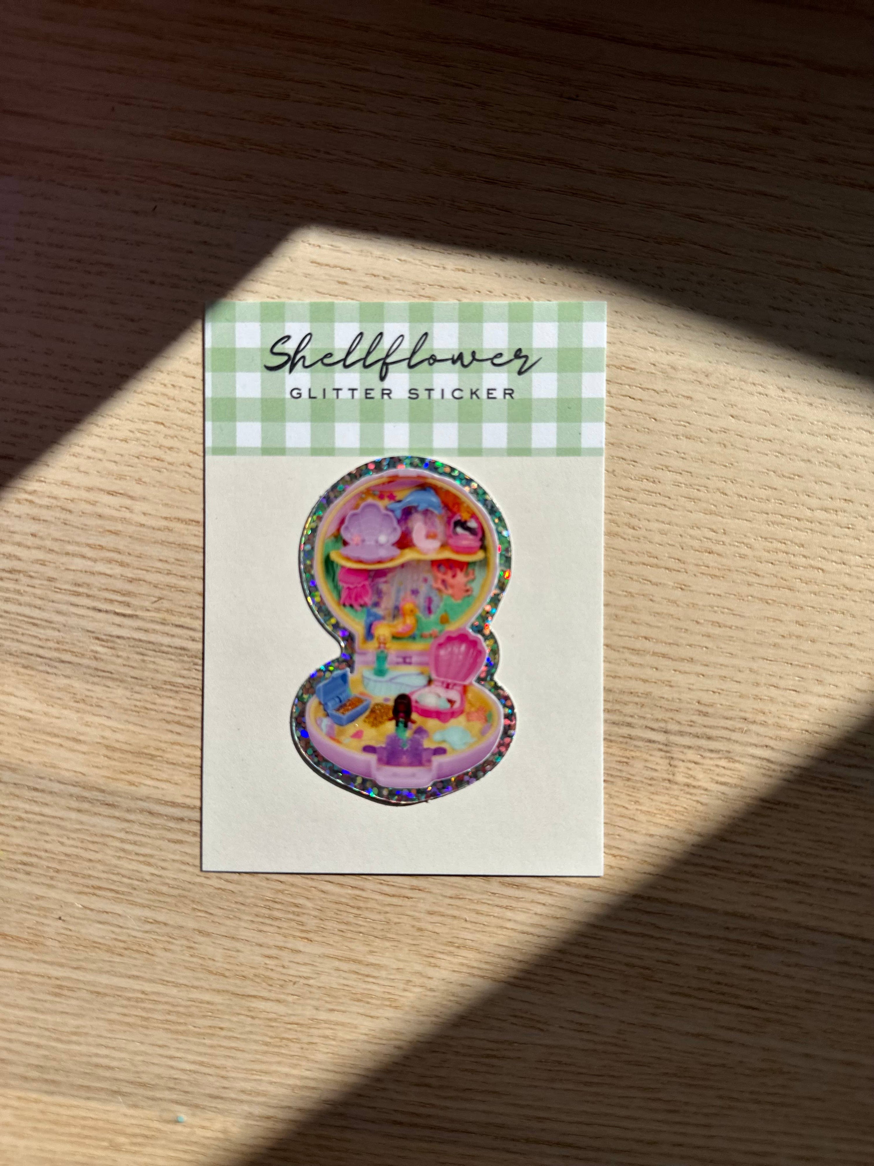Shellflower glitter sticker on a wooden surface with a checkered border