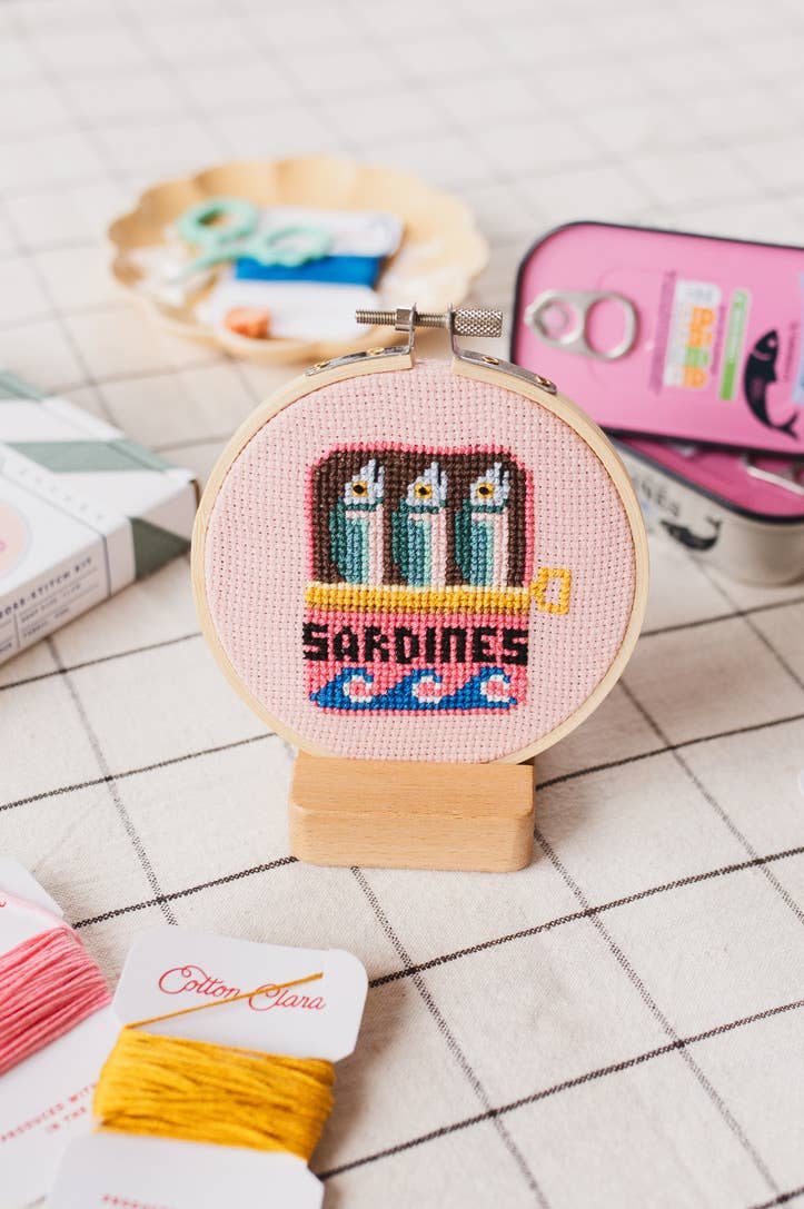 Cross-stitched embroidery hoop with 'Sardines' design on a grid background