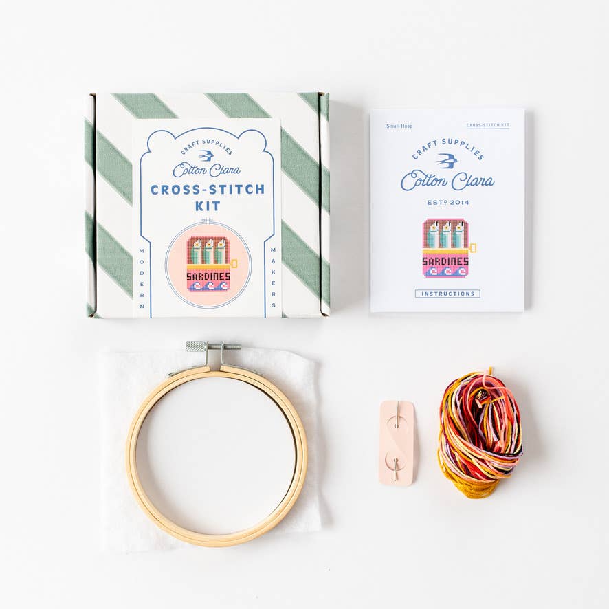 Cross-stitch kit with hoop, thread, and packaging on a white background
