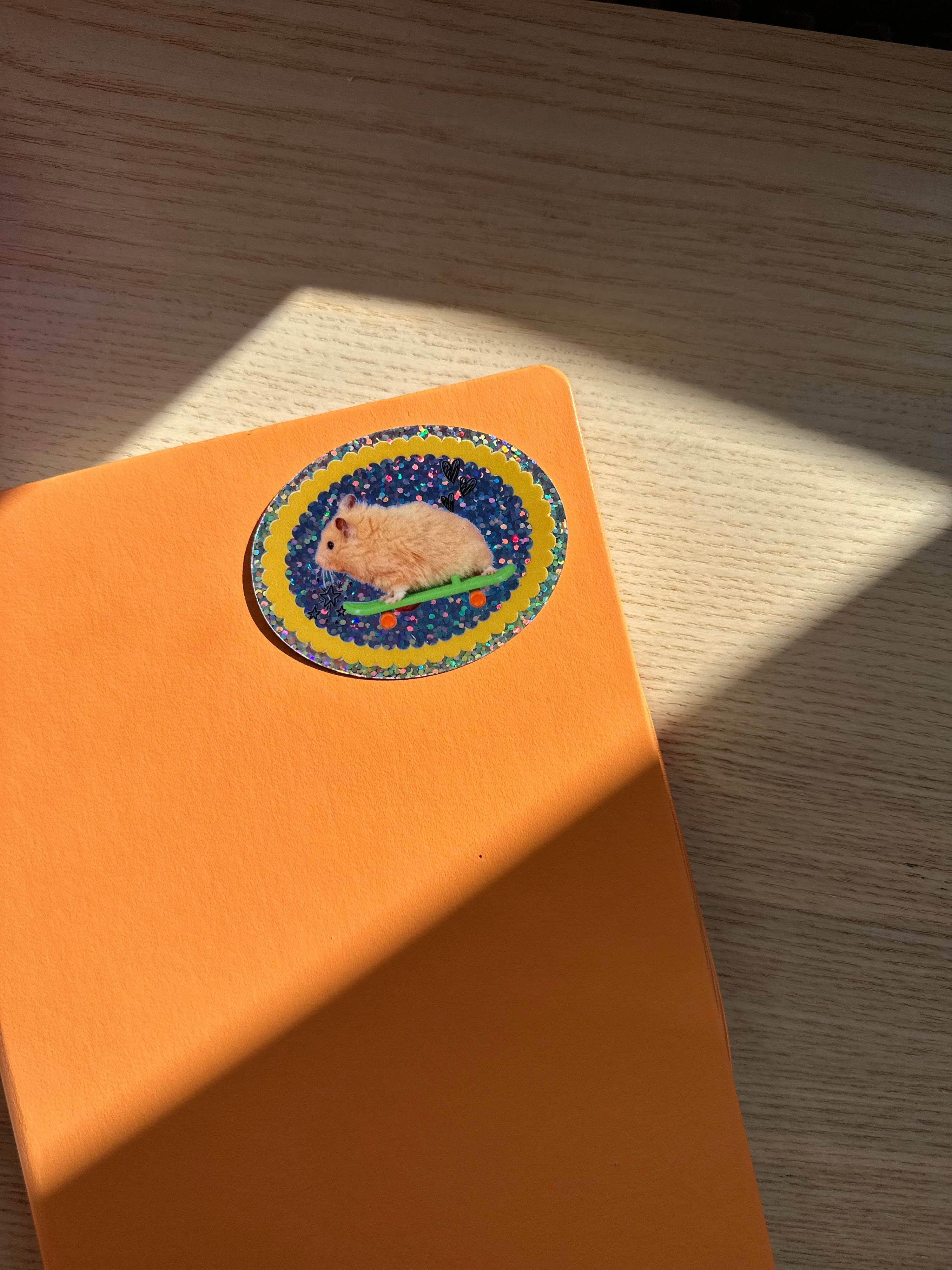 Orange notebook with a colorful sticker of a hamster on a wooden surface