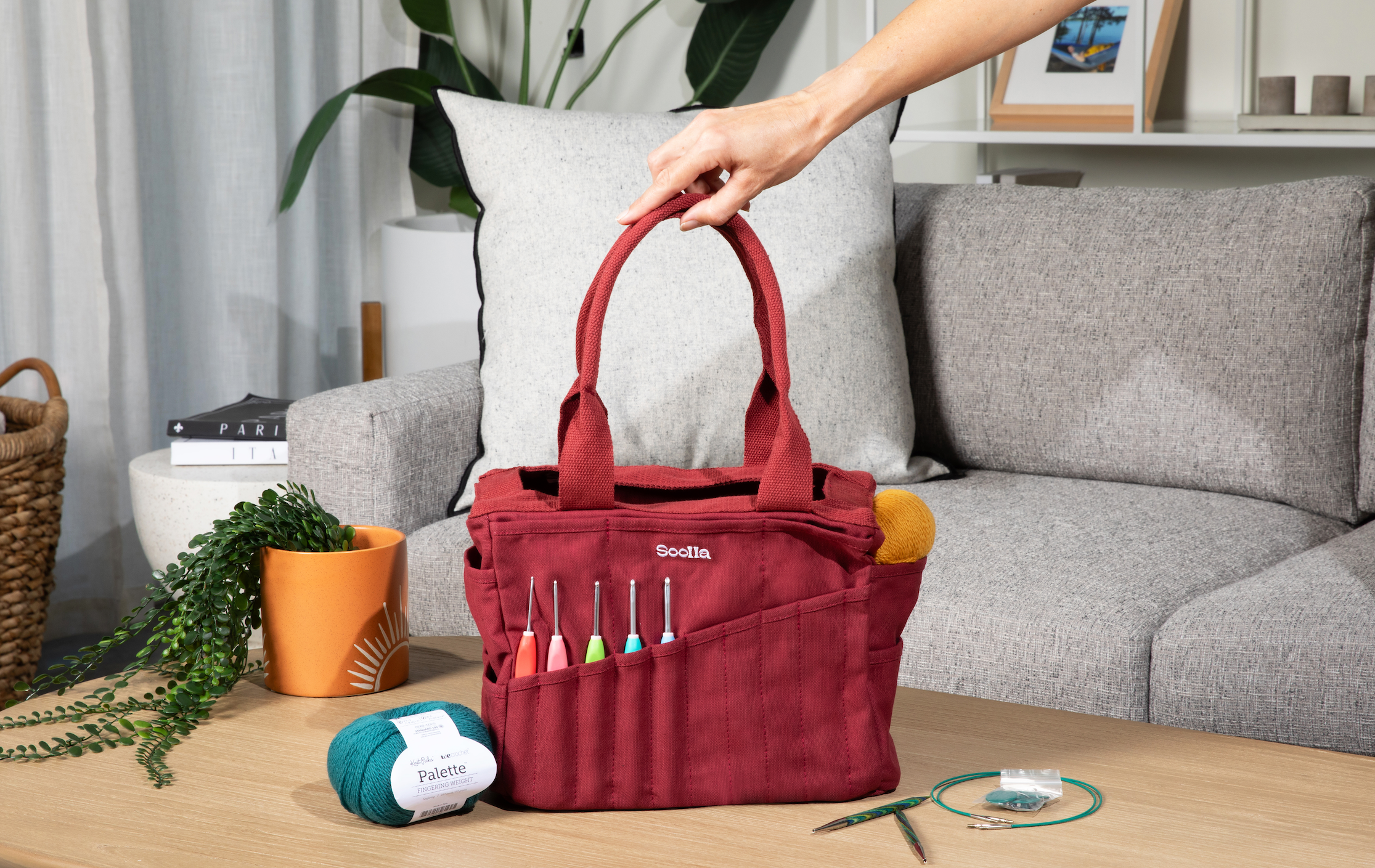Red tote bag with knitting supplies on a table in a living room setting