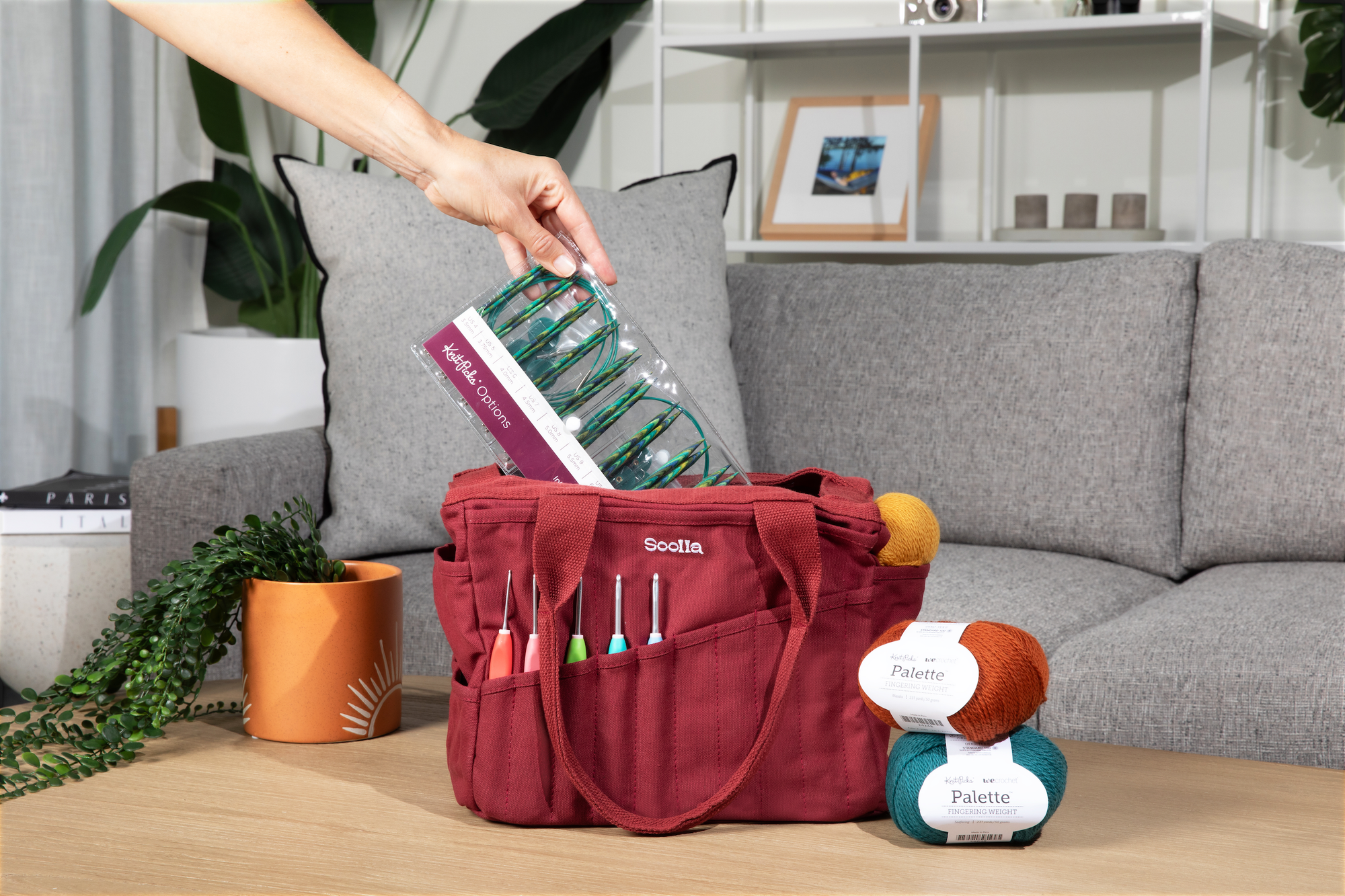 Red craft bag with knitting supplies on a wooden table in a living room setting