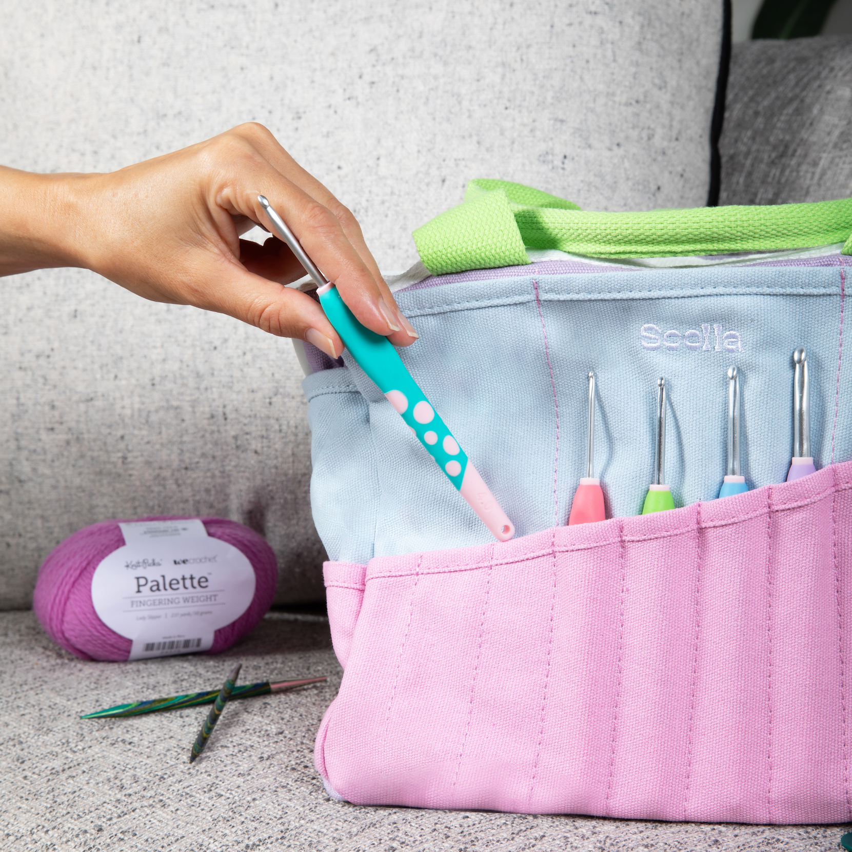 Pink Soolla crochet hook case with various hooks, yarn, and a hand holding a teal and pink hook.