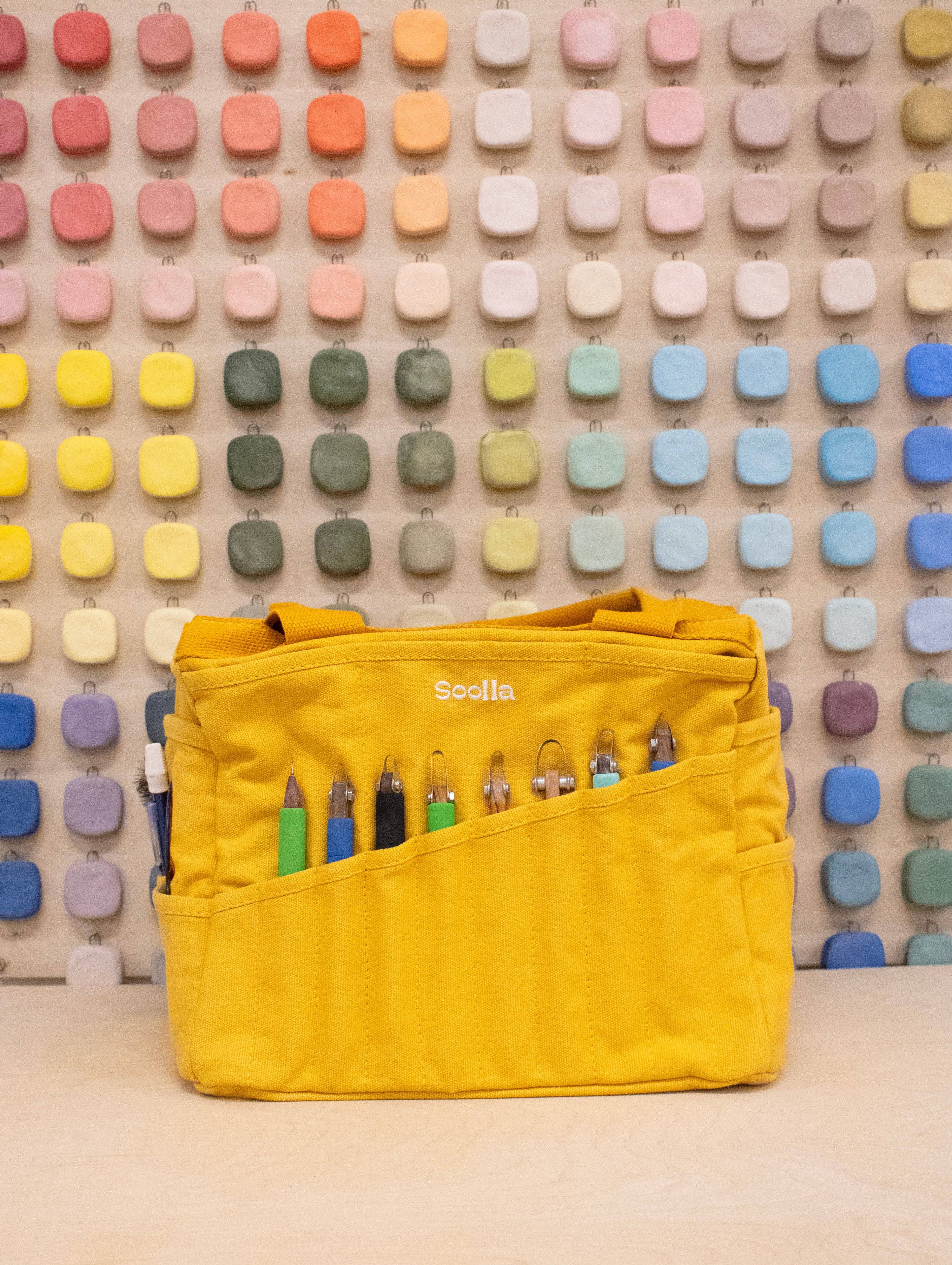 Yellow bag with stationery items against a colorful geometric wall.