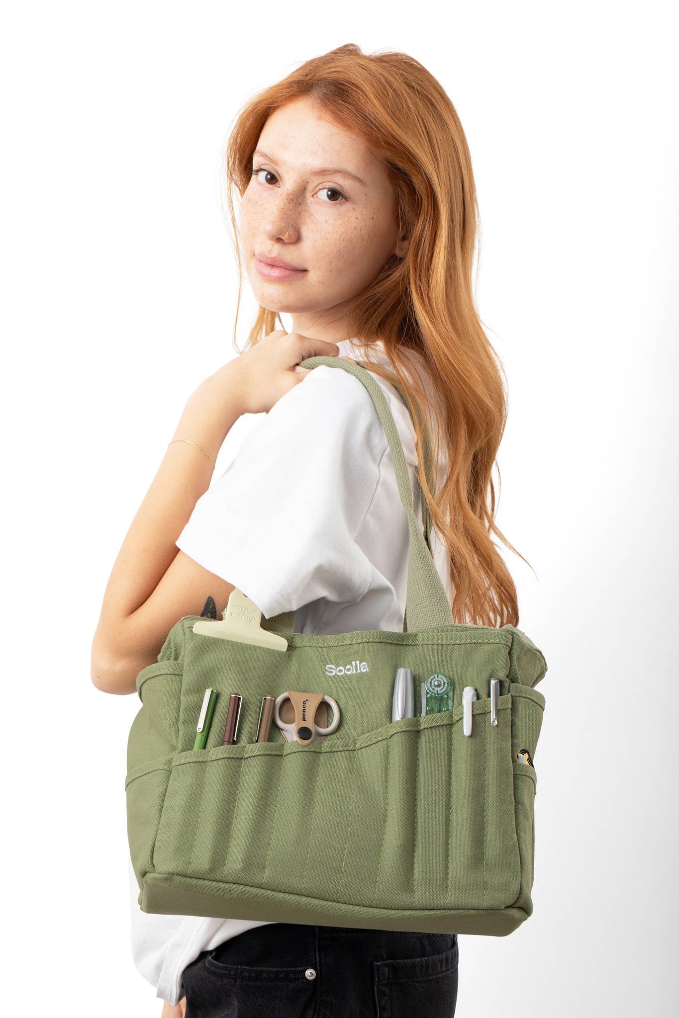 Person holding a green bag with various compartments on a white background