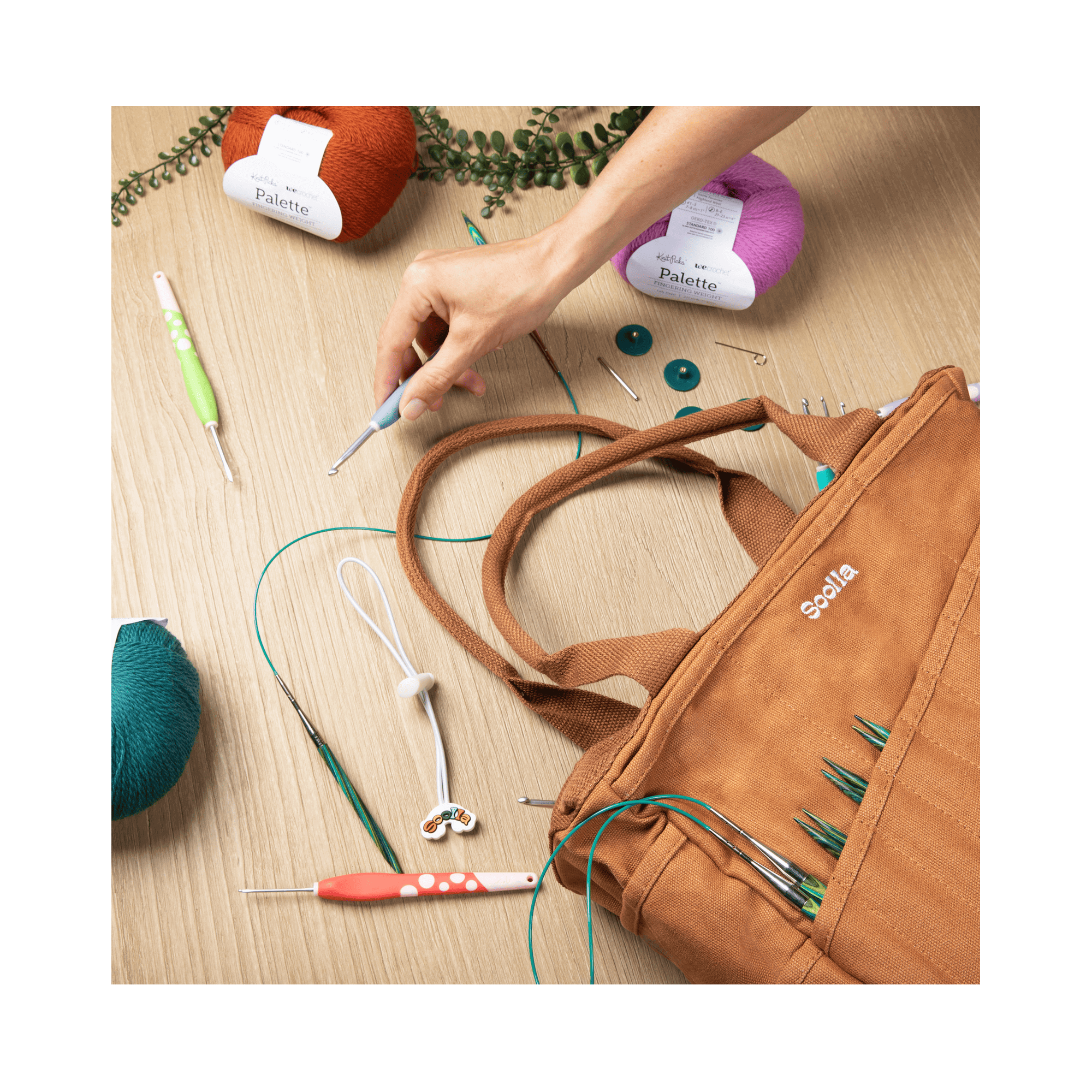 Brown craft bag with knitting tools and yarn on a wooden surface