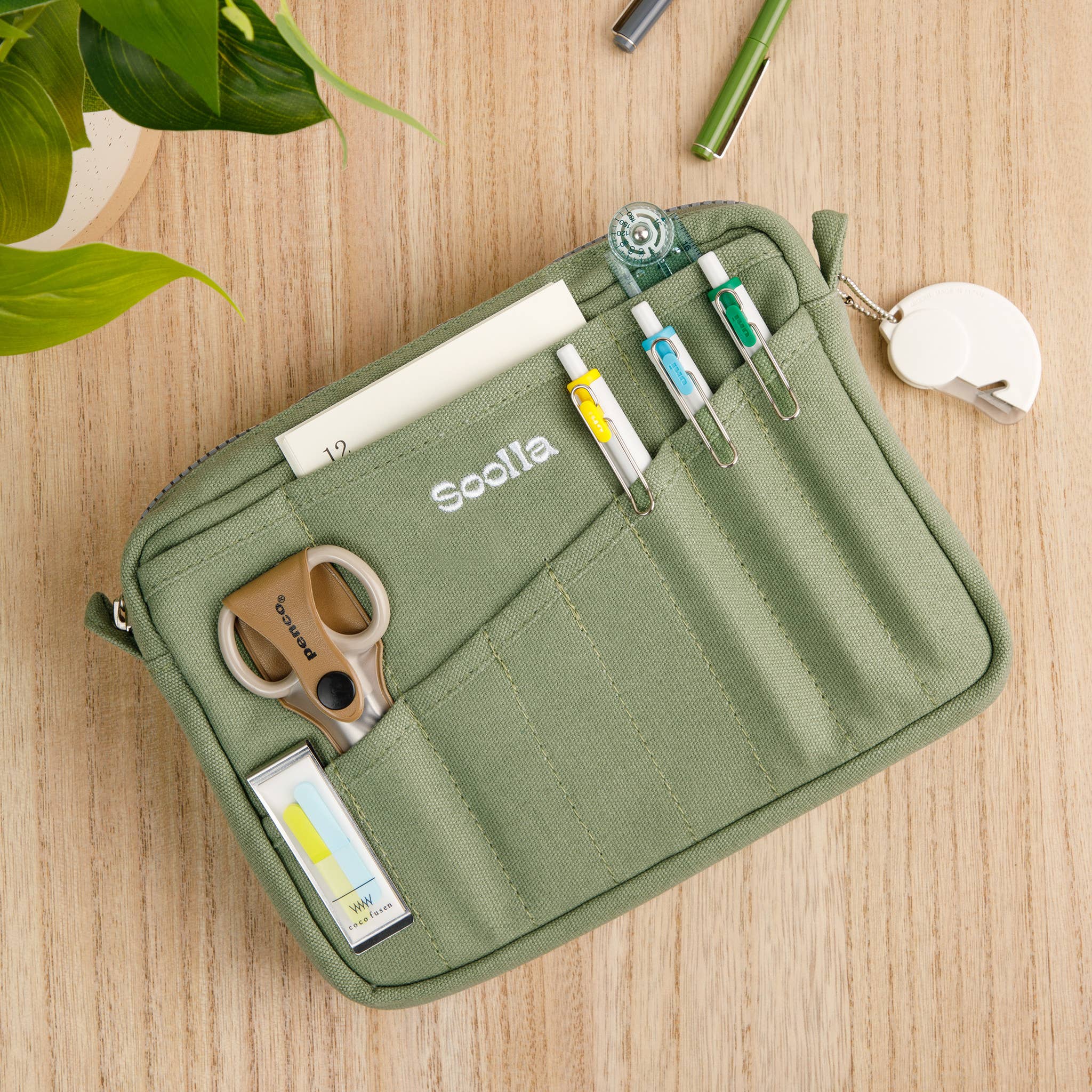 Green Soolla pencil case with stationery items on a wooden surface