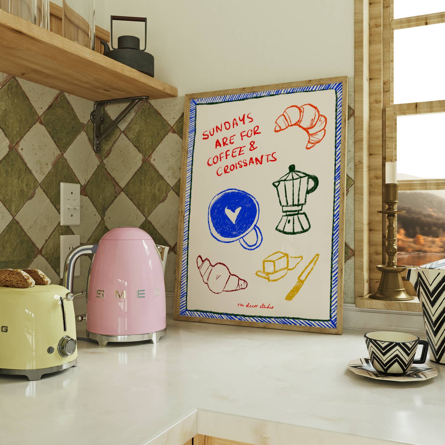 A colorful framed print with the text 'Sundays Are For Coffee & Croissants' displayed on a kitchen counter, with a pink toaster and various kitchen items in the background.