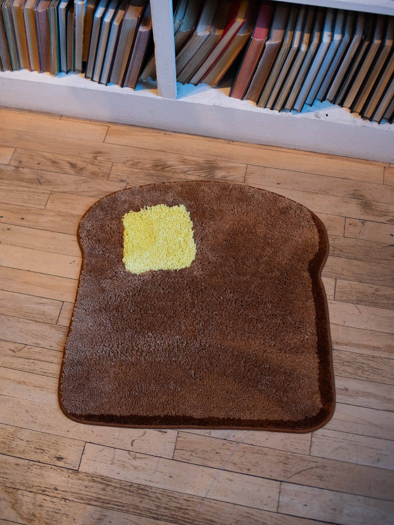 Brown rug shaped like a piece of toast with a yellow square on a wooden floor.