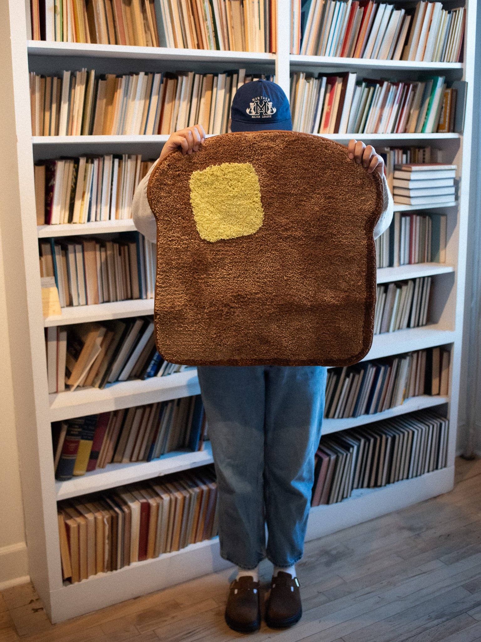 Person holding a brown toast mat with a yellow square in front of a bookshelf