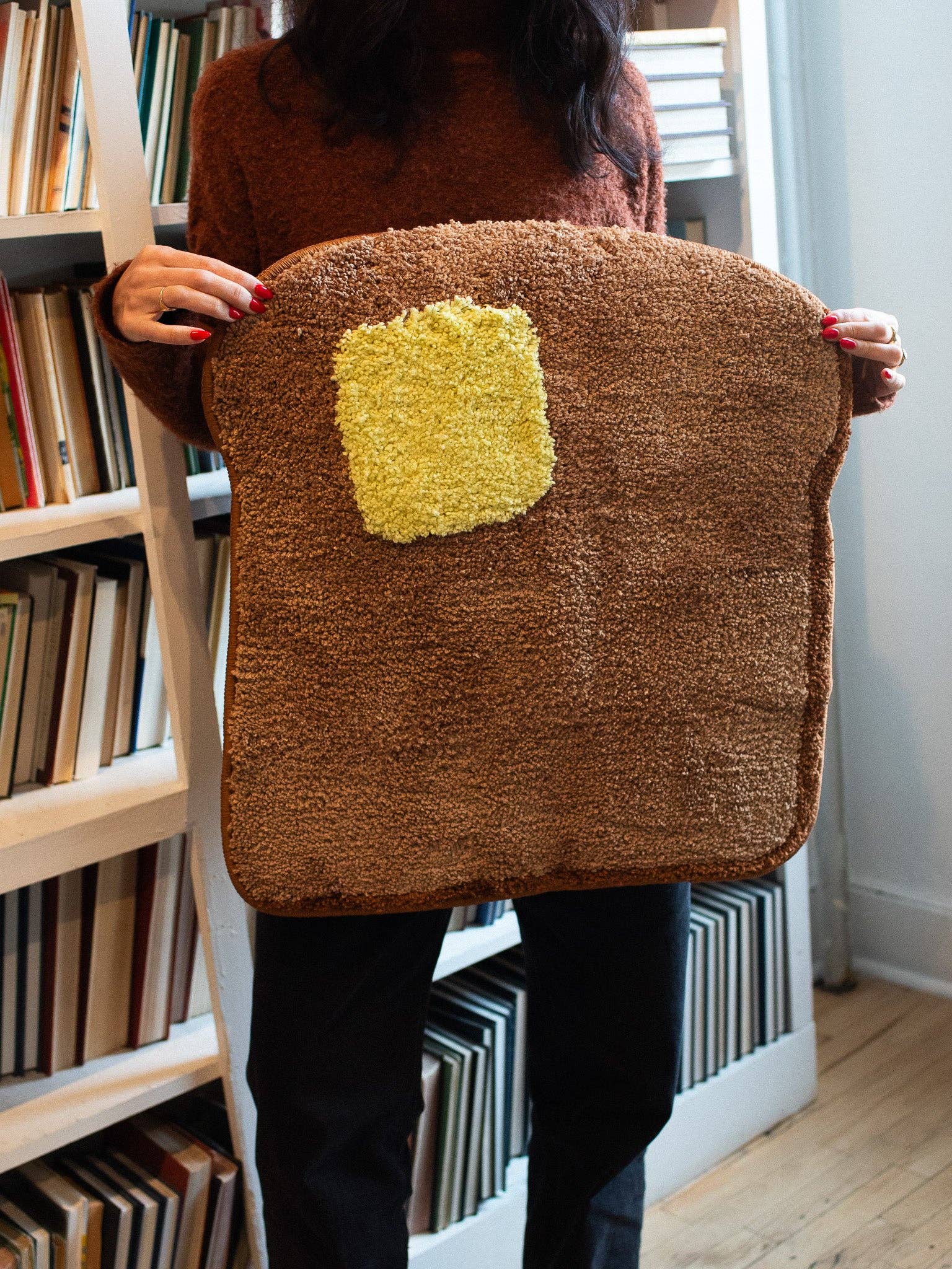 Person holding a brown textured bag with a yellow square patch in front of a bookshelf.