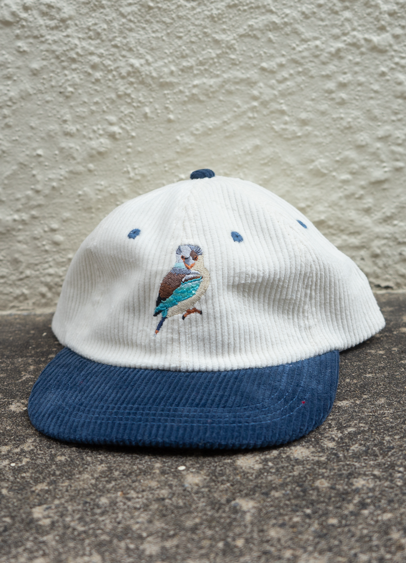 White cap with blue brim and embroidered bird design on a textured surface