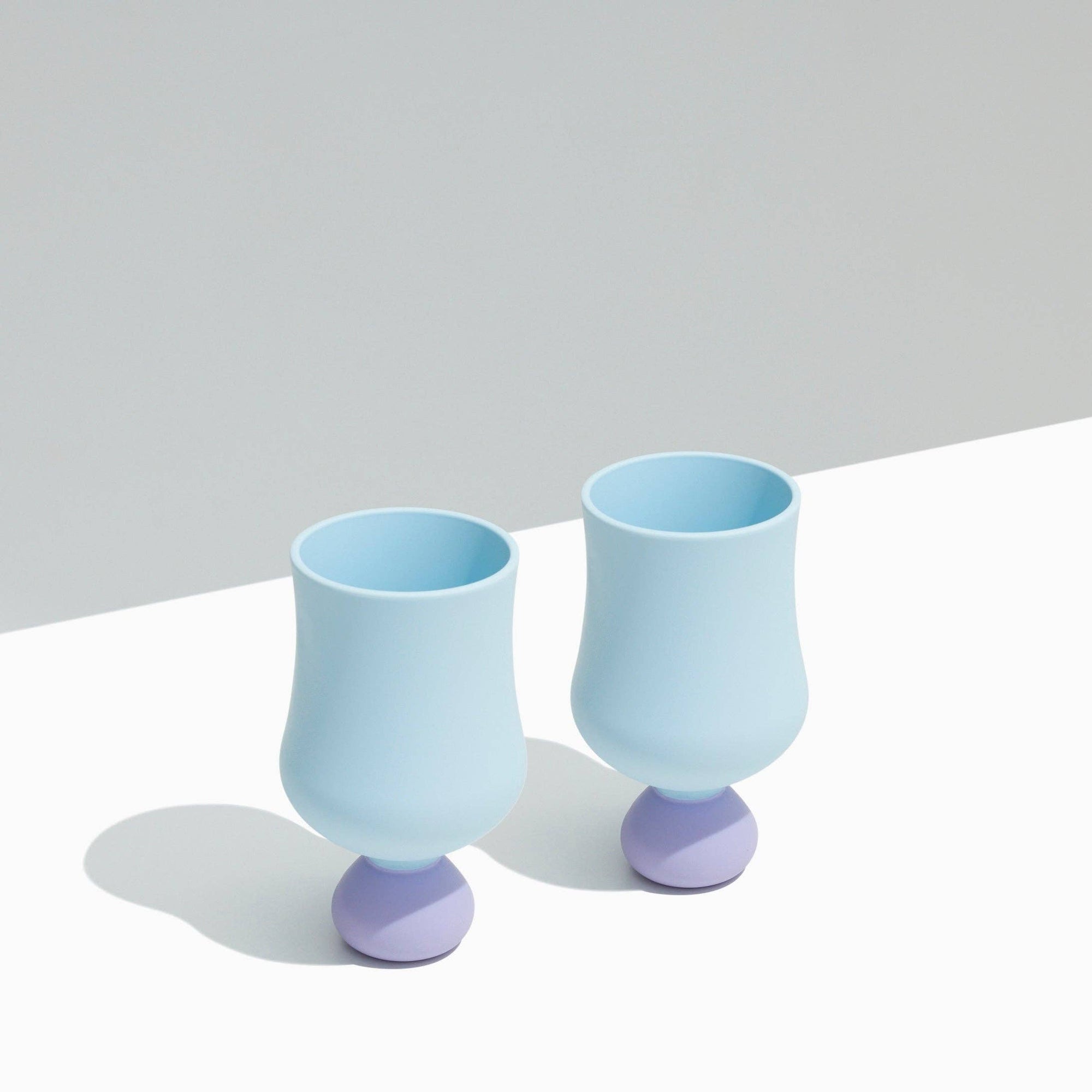 Two light blue silicone cups with purple bases on a white surface.