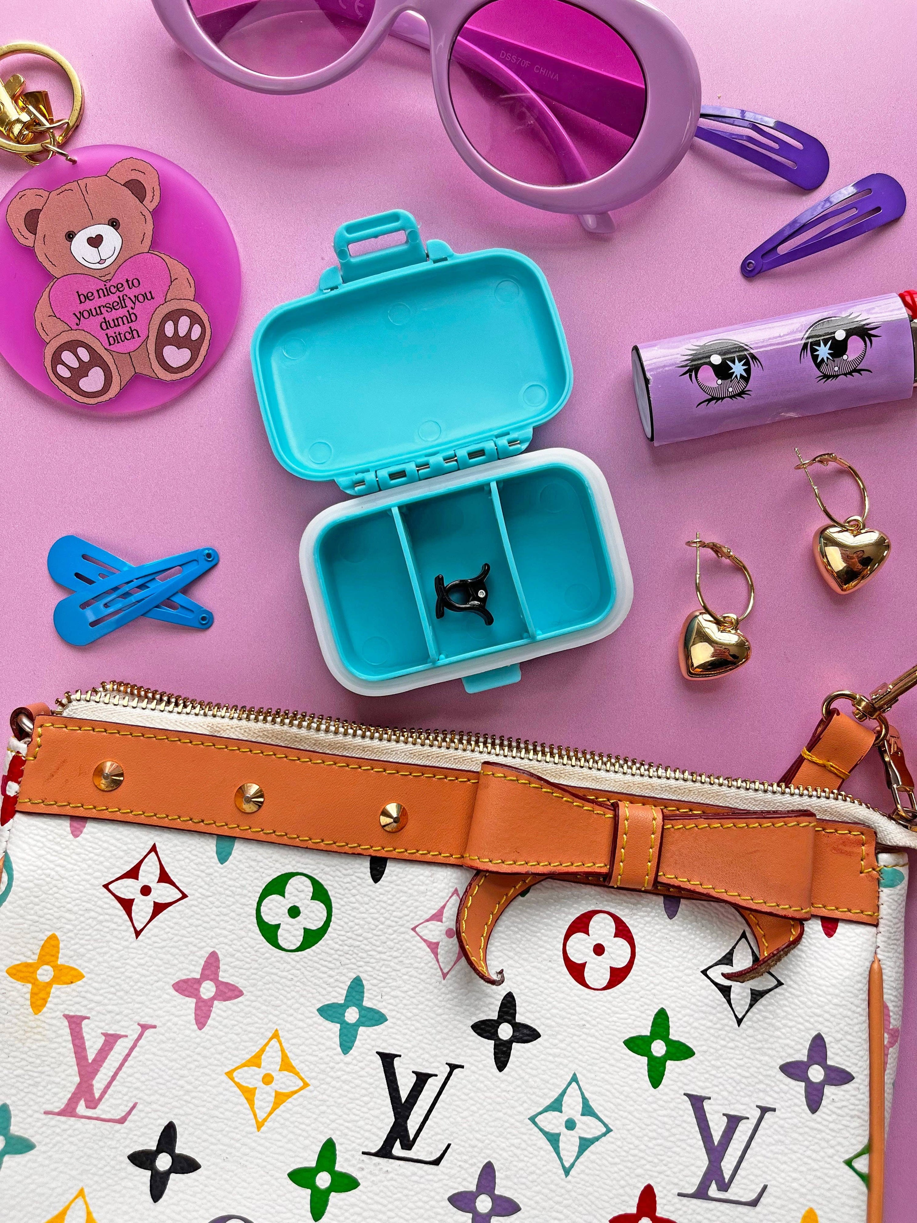 Colorful accessories including a blue container, teddy bear keychain, sunglasses, hair clips, and a patterned handbag on a pink background.