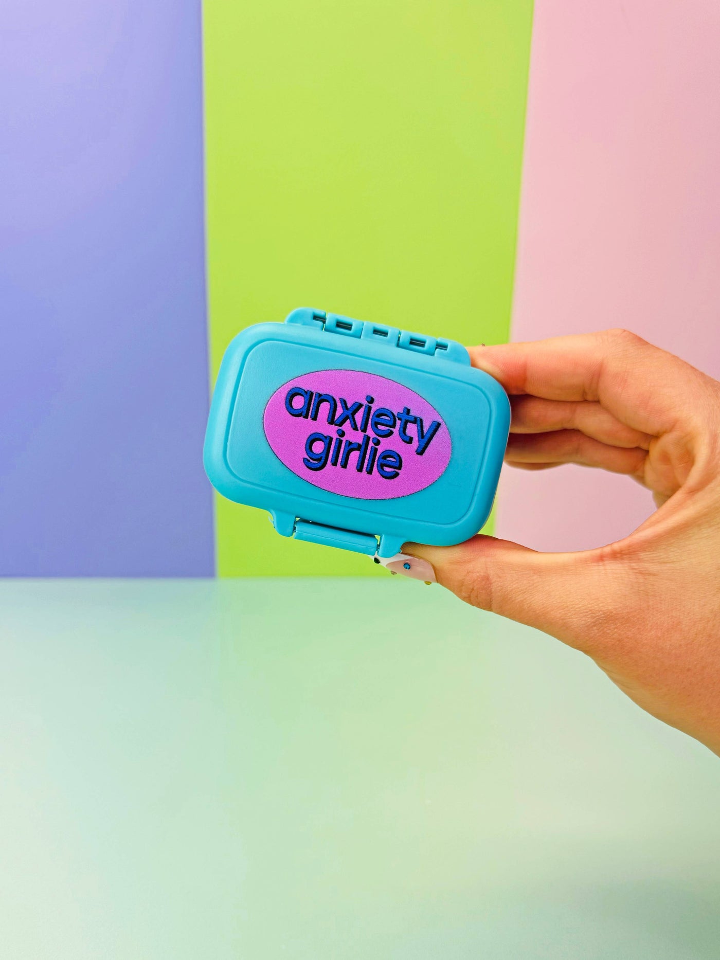 Hand holding a blue 'anxiety girl' box against a colorful background