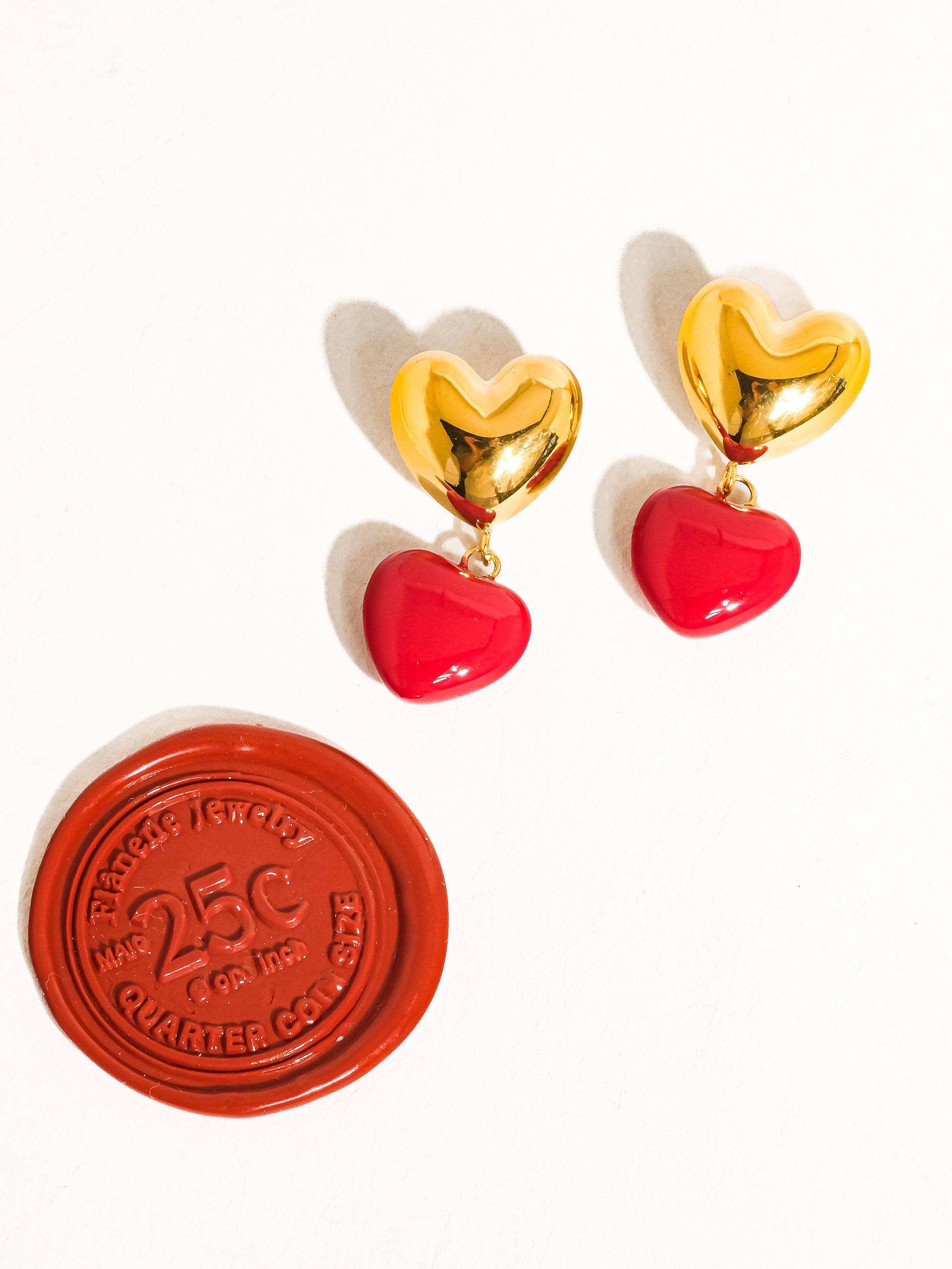 Gold heart-shaped earrings with red accents on a white background