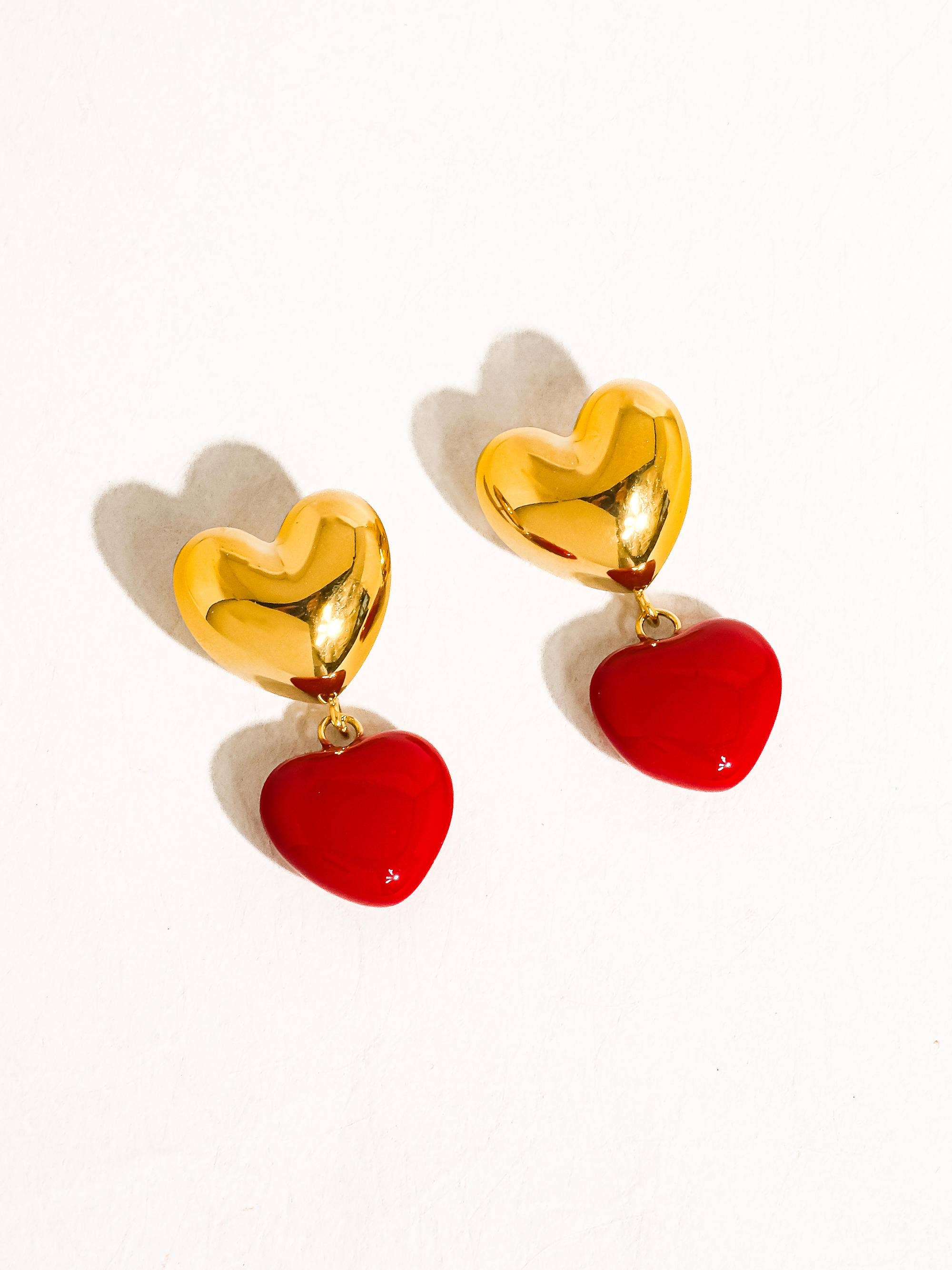 Gold heart-shaped earrings with red bottoms on a white background