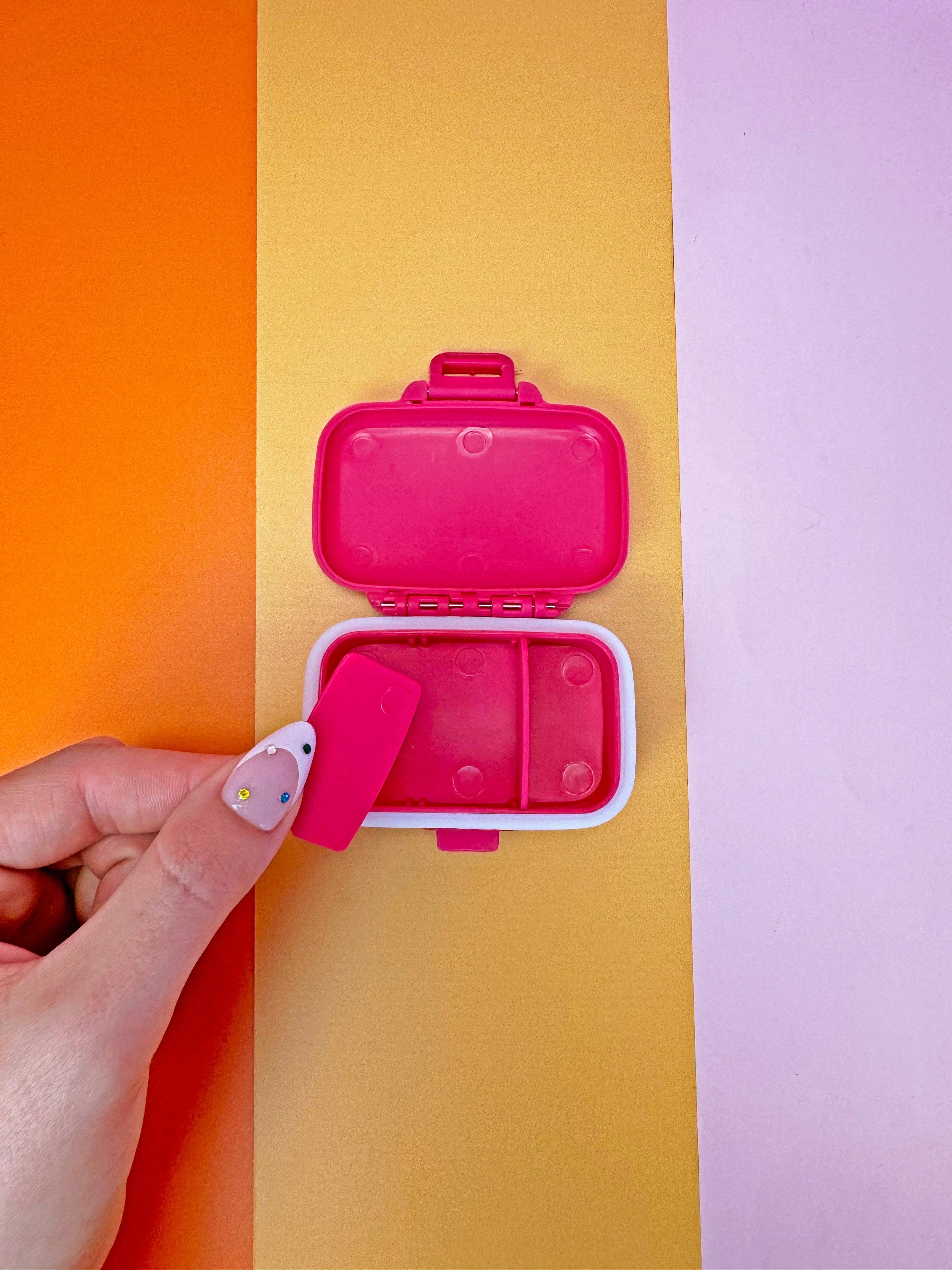 Pink bento box with a lid held by a hand against a colorful background