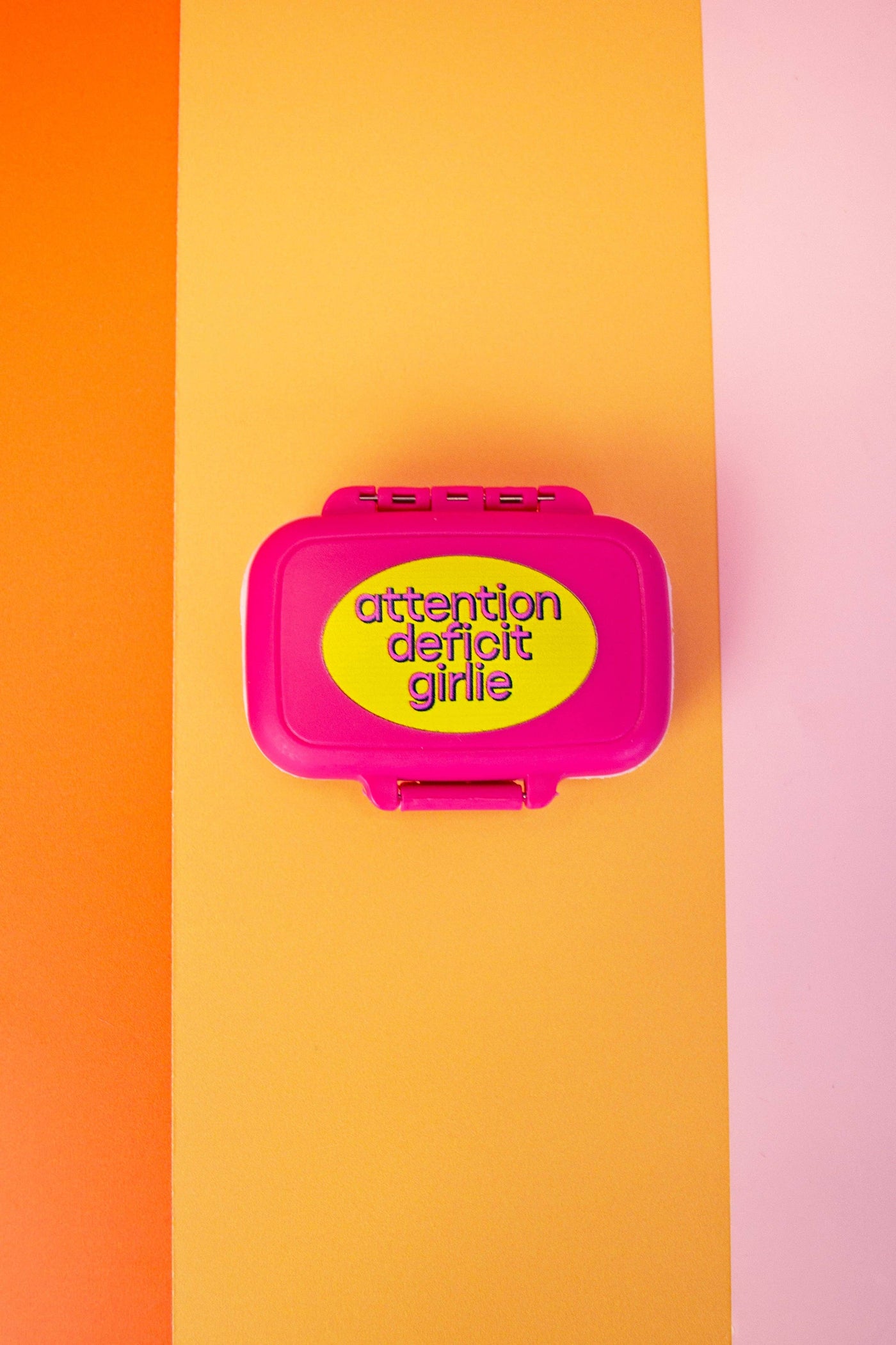Pink lunch box with yellow label on an orange and pink striped background
