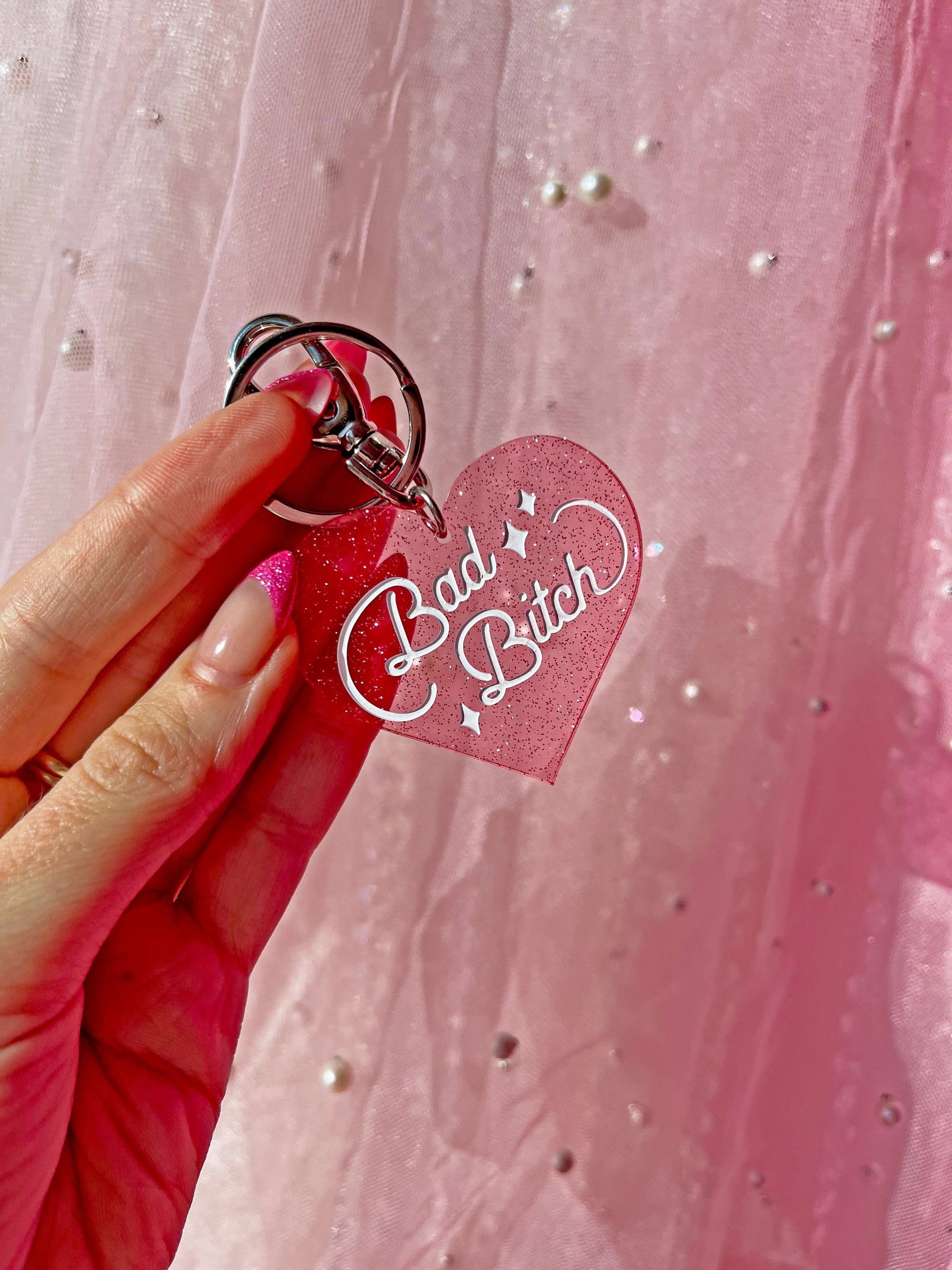 Heart-shaped keychain with 'Bad Bitch' text held against a pink background