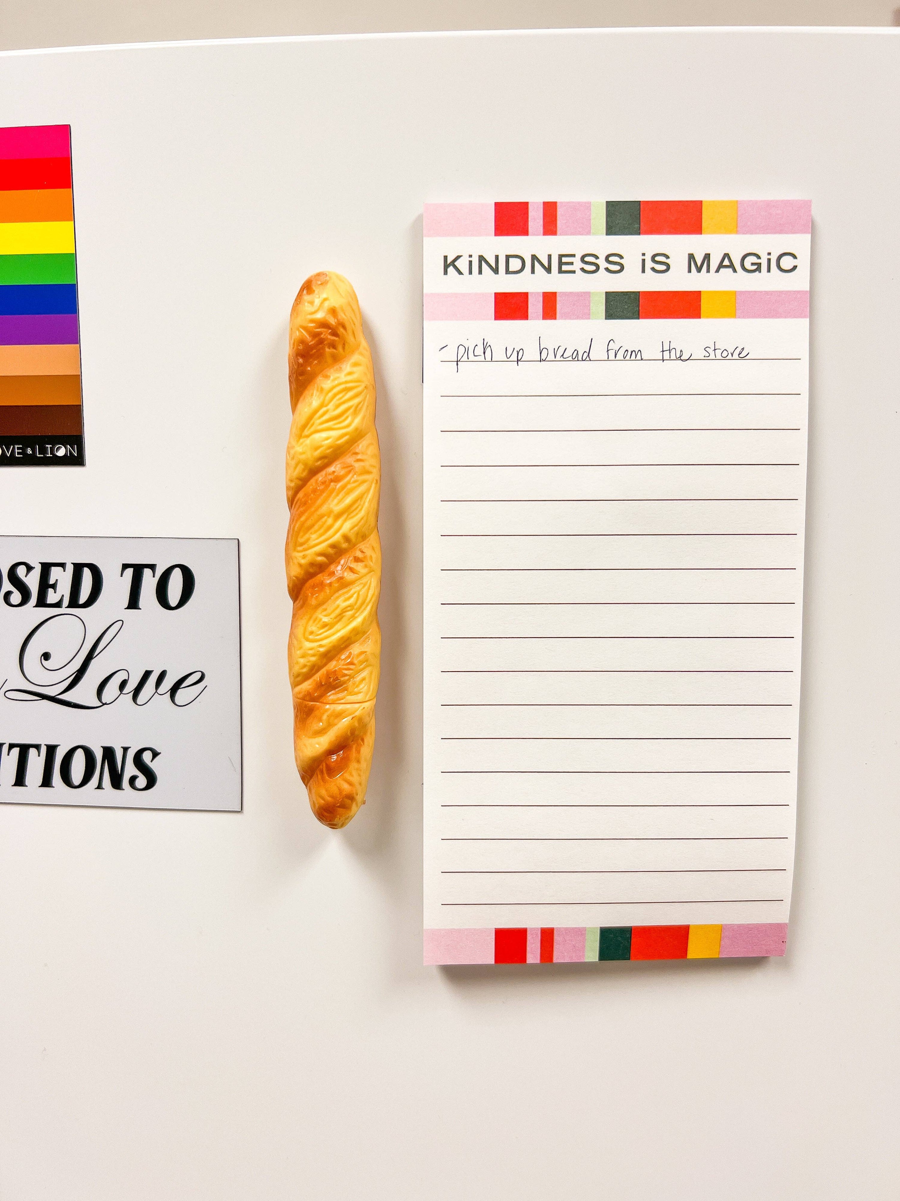 Notepad with 'Kindness is Magic' text and a croissant on a white surface.