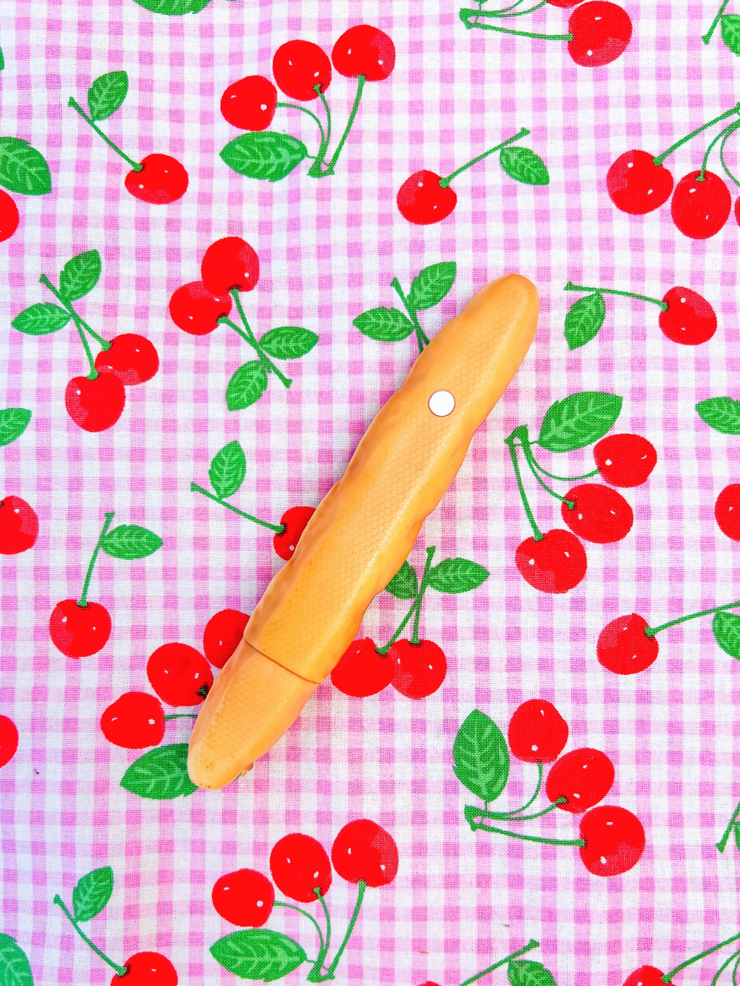 Orange cylindrical object on a pink gingham background with red cherries and green leaves.