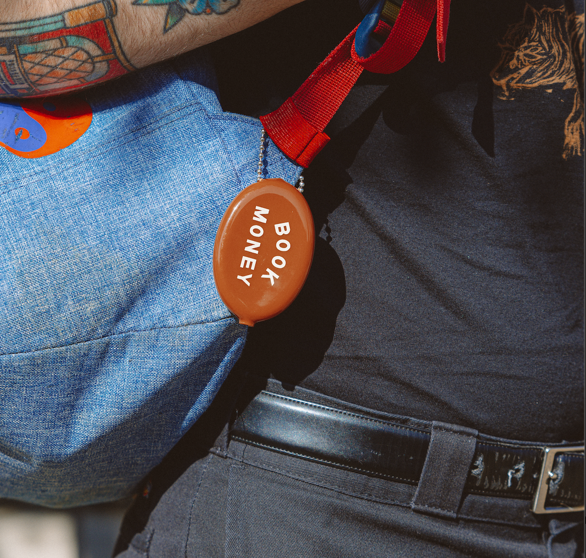 Person wearing a blue backpack with a red strap and an orange 'Book Money' badge.