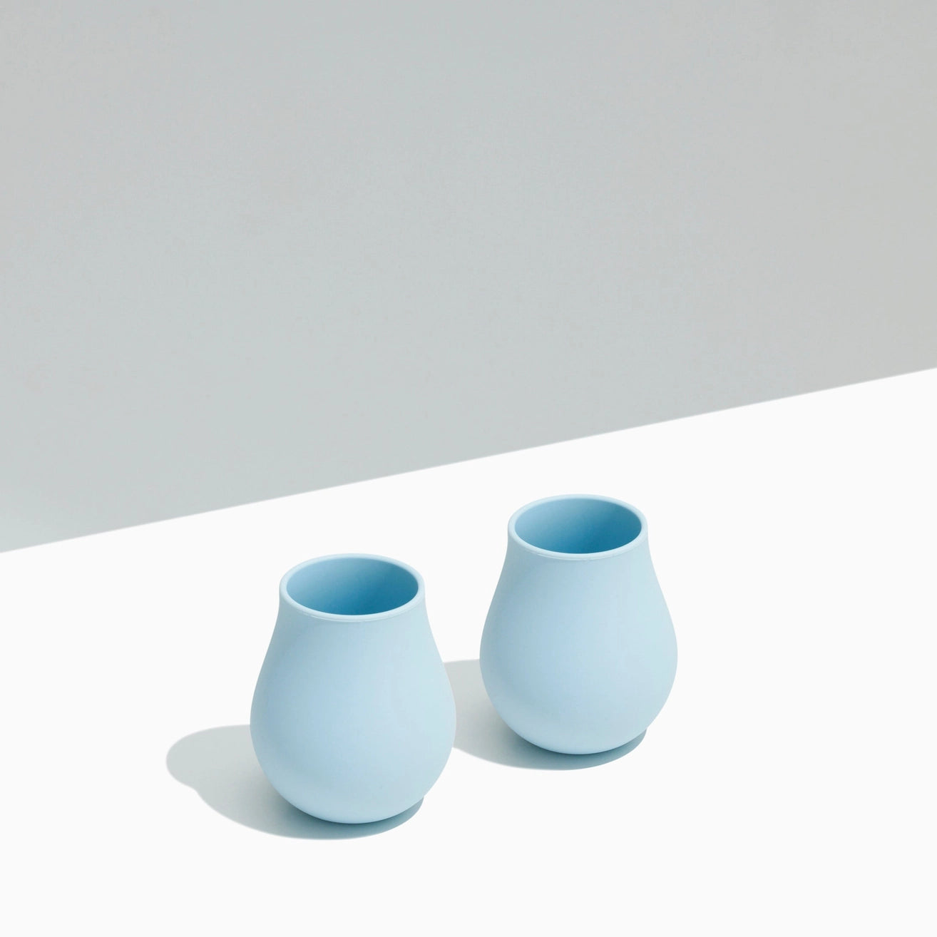 Two light blue ceramic cups on a white surface with a gray background