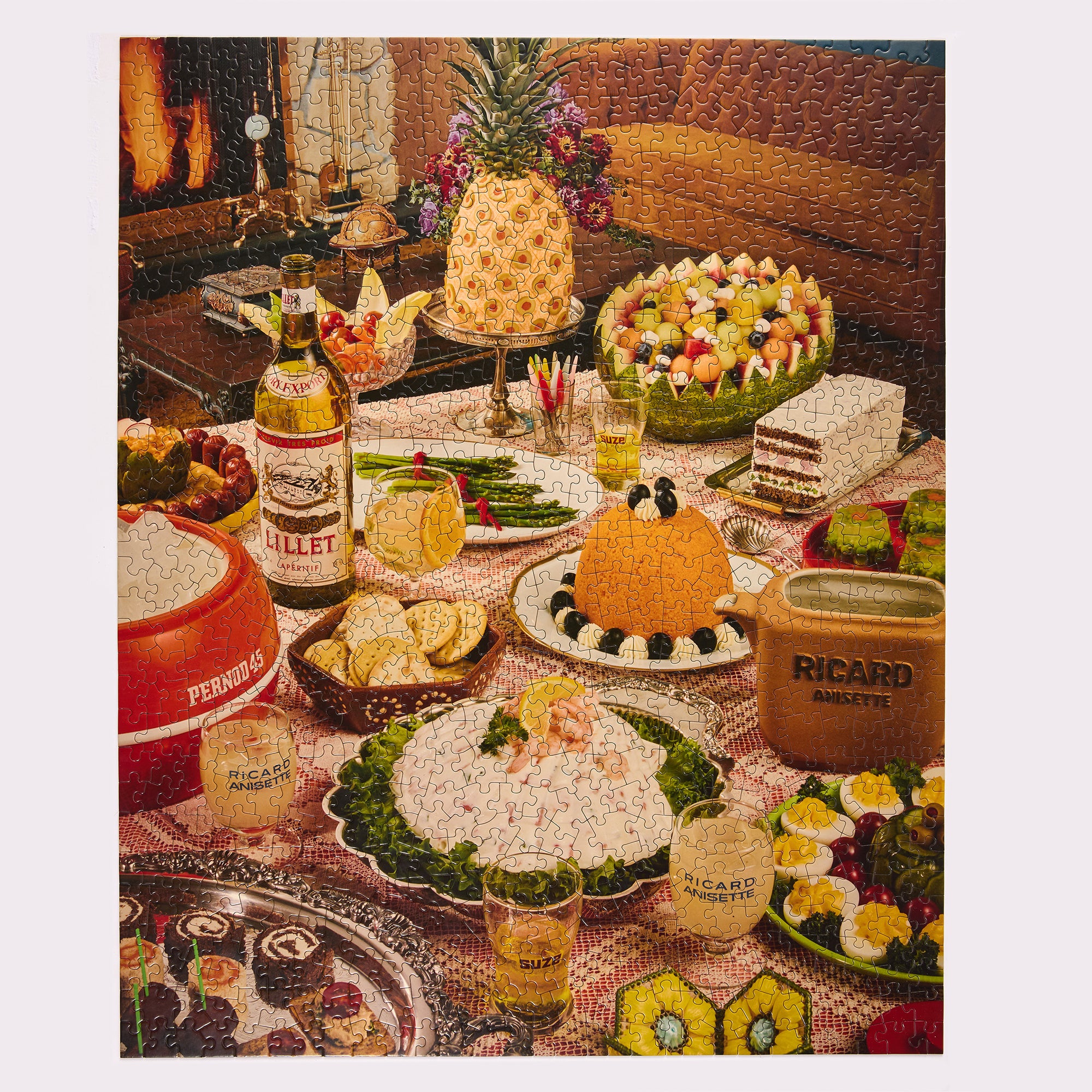 A vintage-style jigsaw party spread with assorted foods and branded containers on a table. Visible products include a bottle labeled RITZEL, a red container labeled PERRINDE, and a brown carton labeled RICARD SOUVENTS, alongside dishes such as a pineapple, fruit salad, cheese, and garnished appetizers.