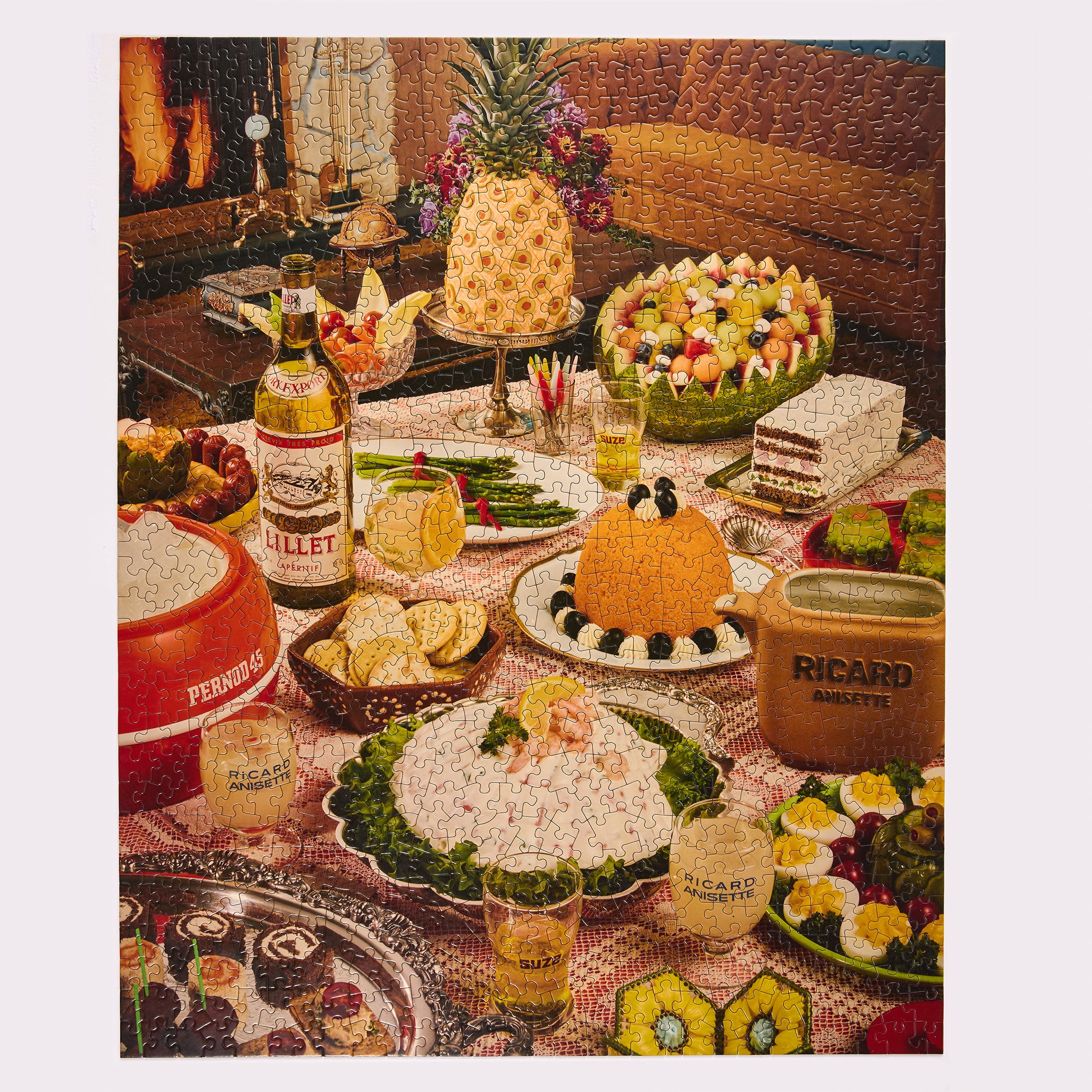 A vintage-style jigsaw party spread with assorted foods and branded containers on a table. Visible products include a bottle labeled RITZEL, a red container labeled PERRINDE, and a brown carton labeled RICARD SOUVENTS, alongside dishes such as a pineapple, fruit salad, cheese, and garnished appetizers.