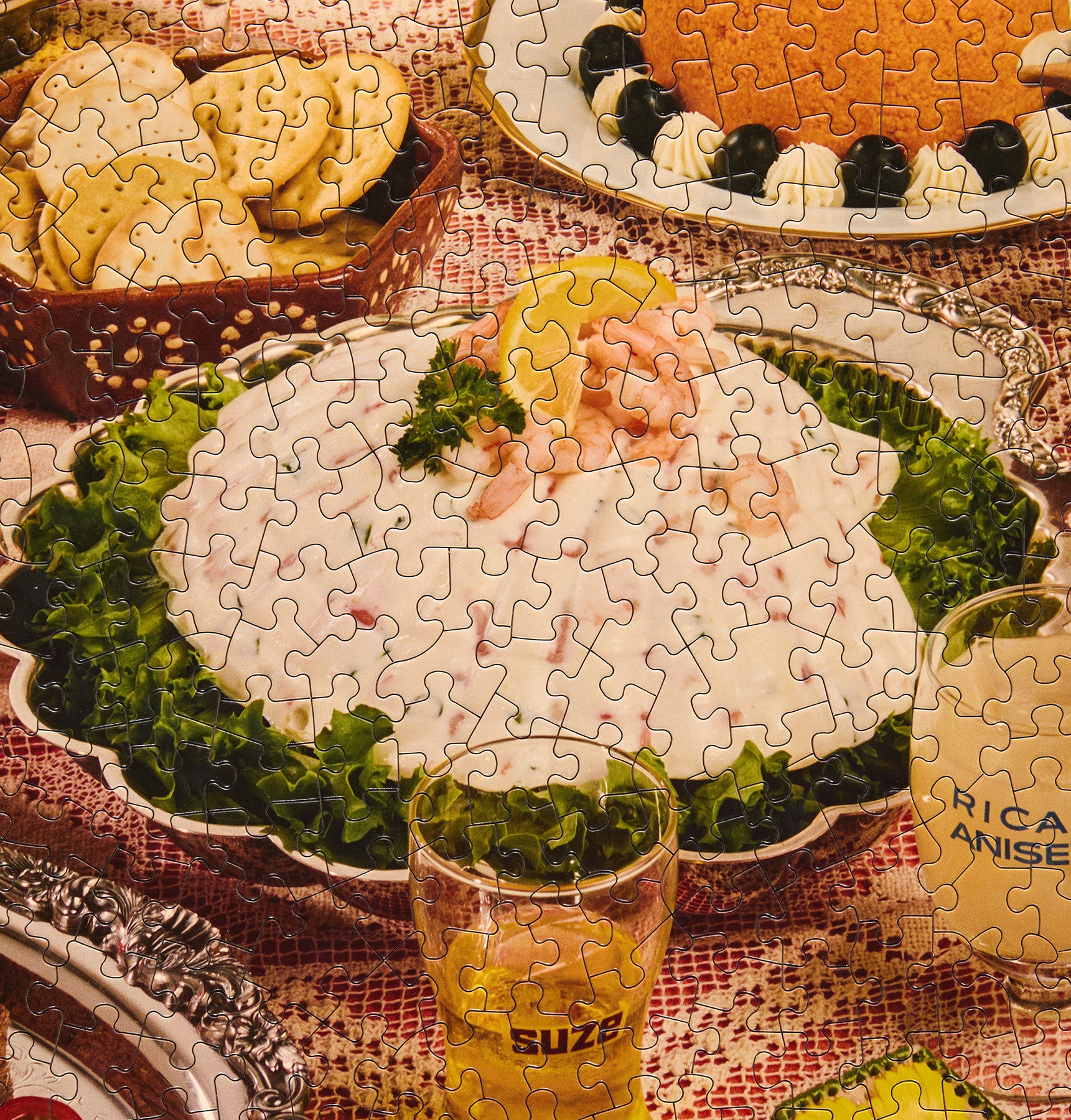 A completed jigsaw puzzle depicting a festive table setting with a large white salad on a bed of green lettuce, pink salmon, and a lemon wedge, surrounded by plates and glasses on a patterned tablecloth.