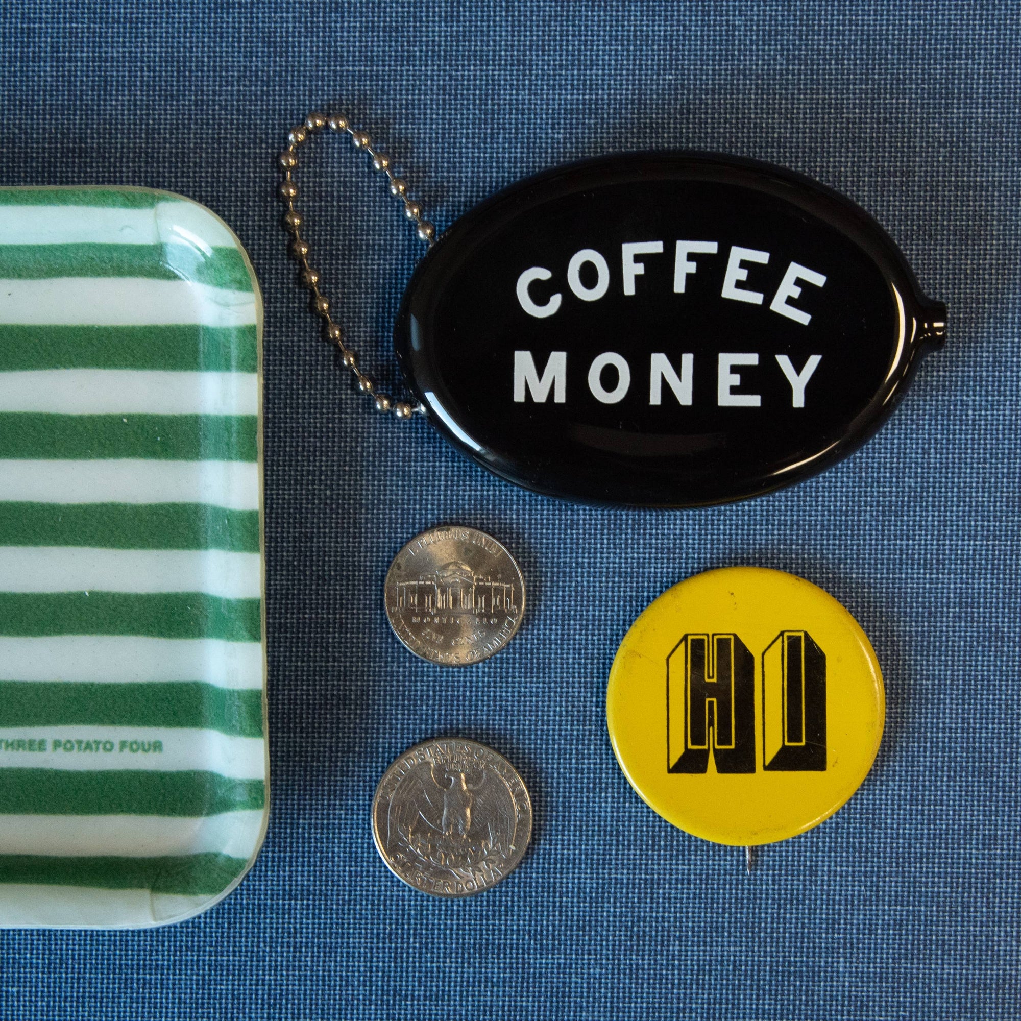 Small pouch, coins, 'Coffee Money' keychain, and yellow button with logo on a blue textured background