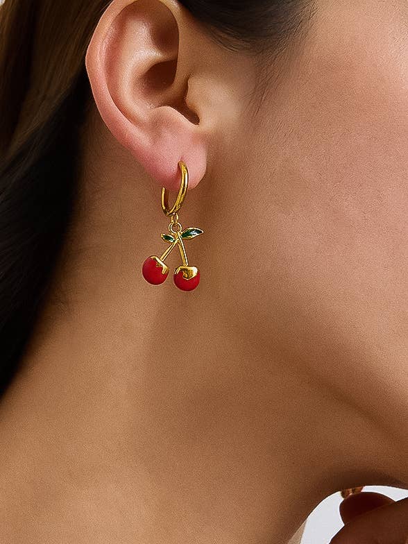 Close-up of a gold earring with cherry charms worn by a person.