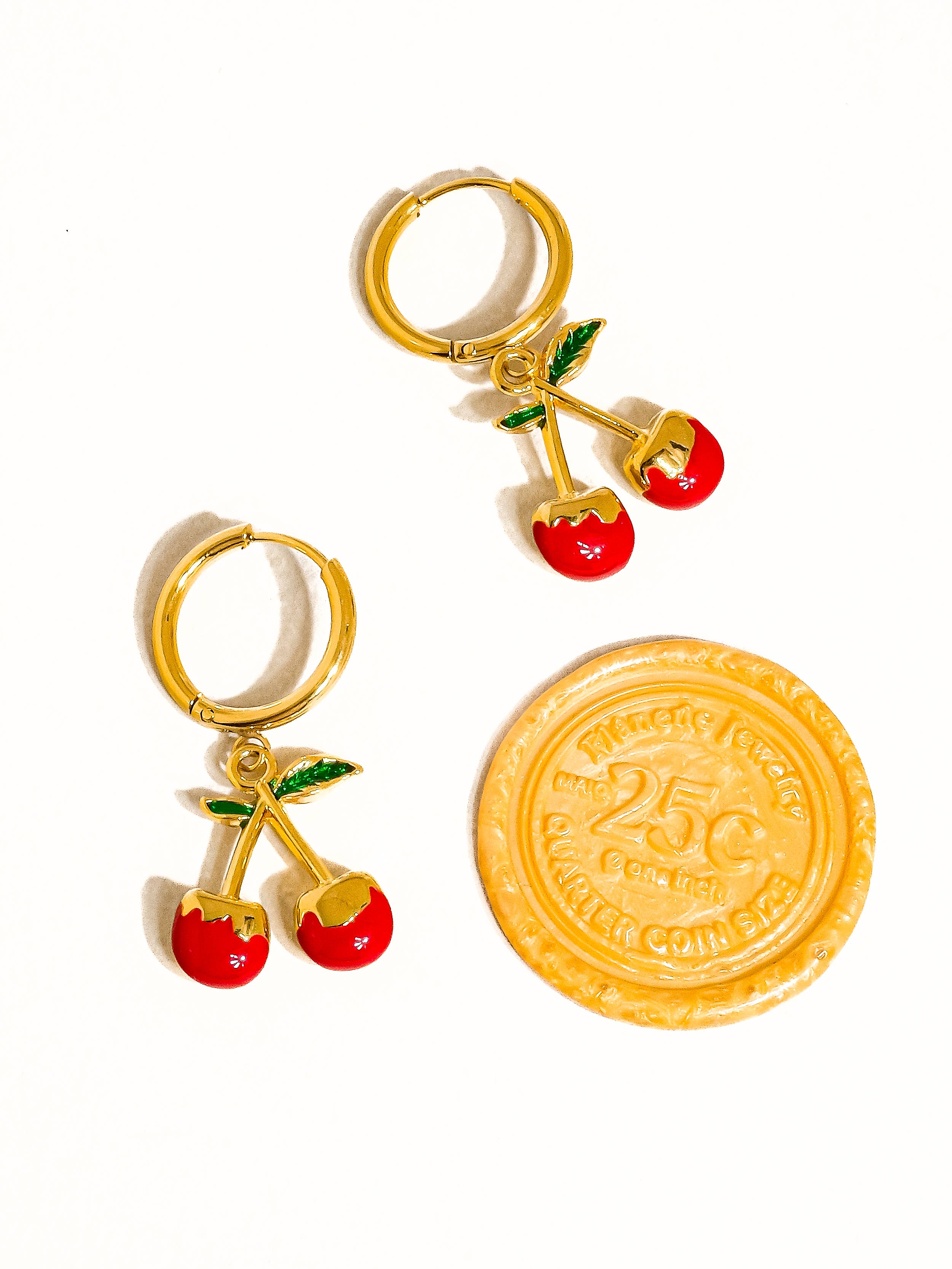 Gold hoop earrings with cherry charms and a yellow coin on a white background
