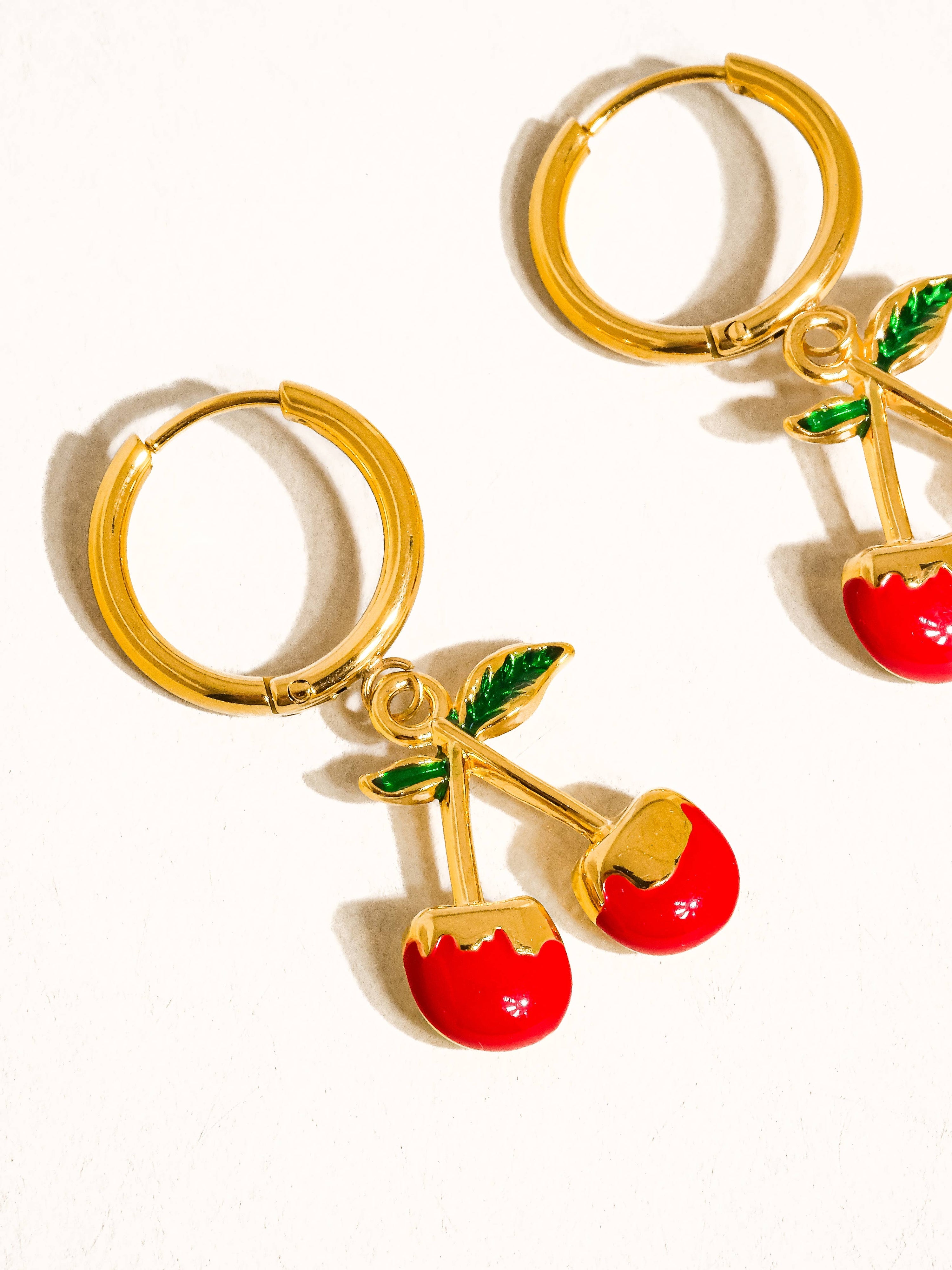 Gold hoop earrings with cherry charms on a white background