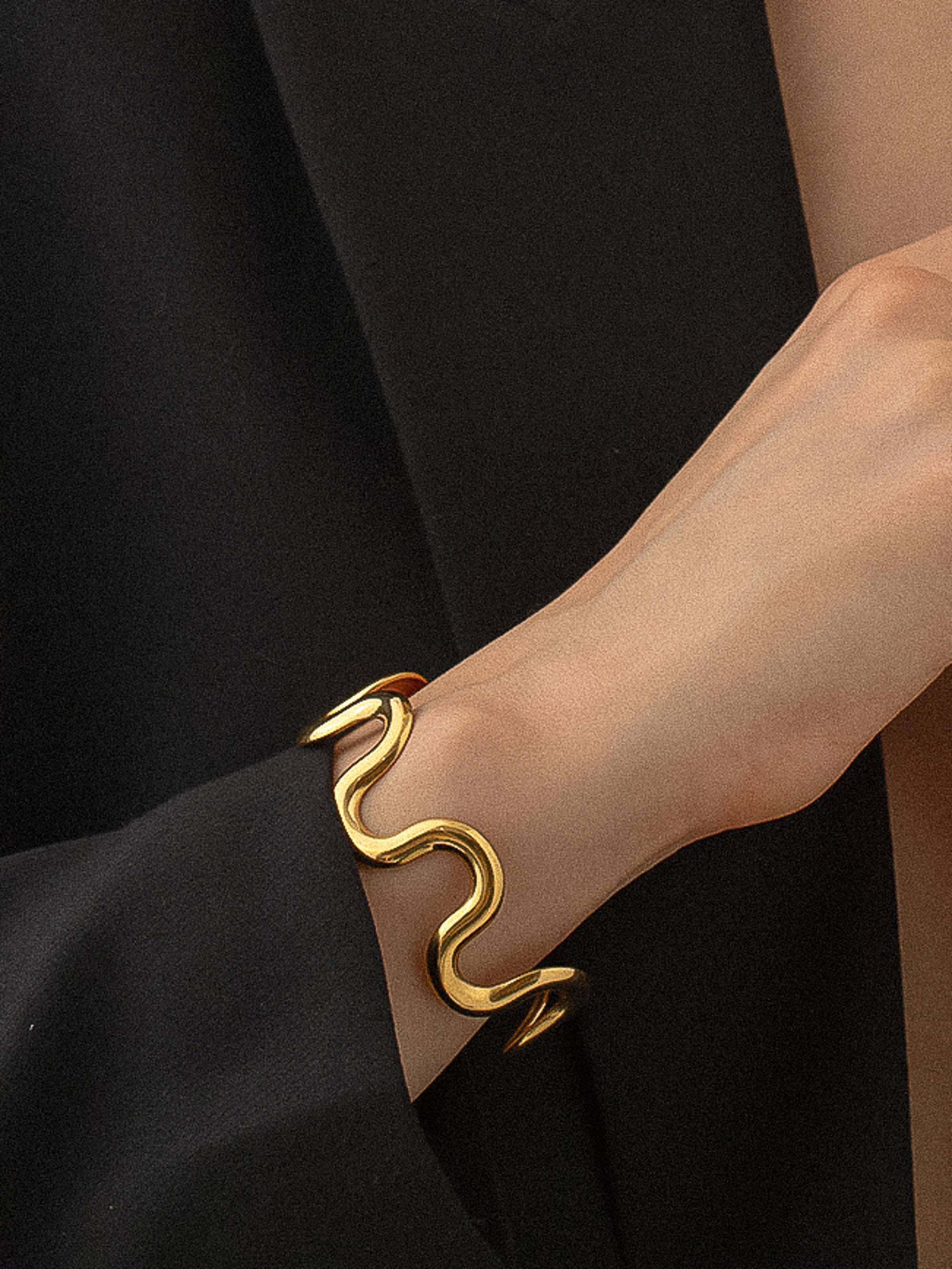 Gold bracelet on a person's wrist against a black background