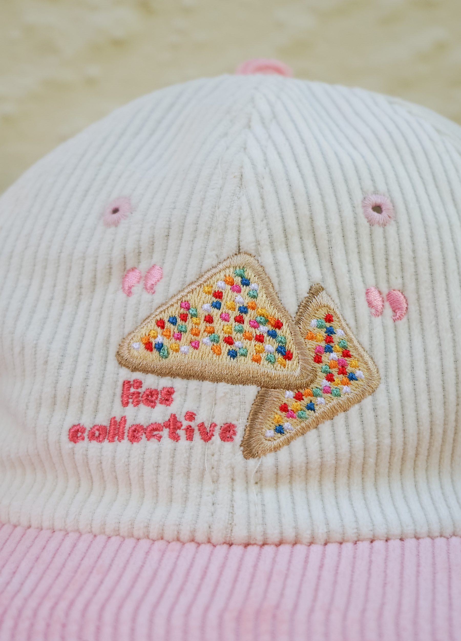 Pink and white cap with colorful embroidered design and 'Her Collective' text on a light background