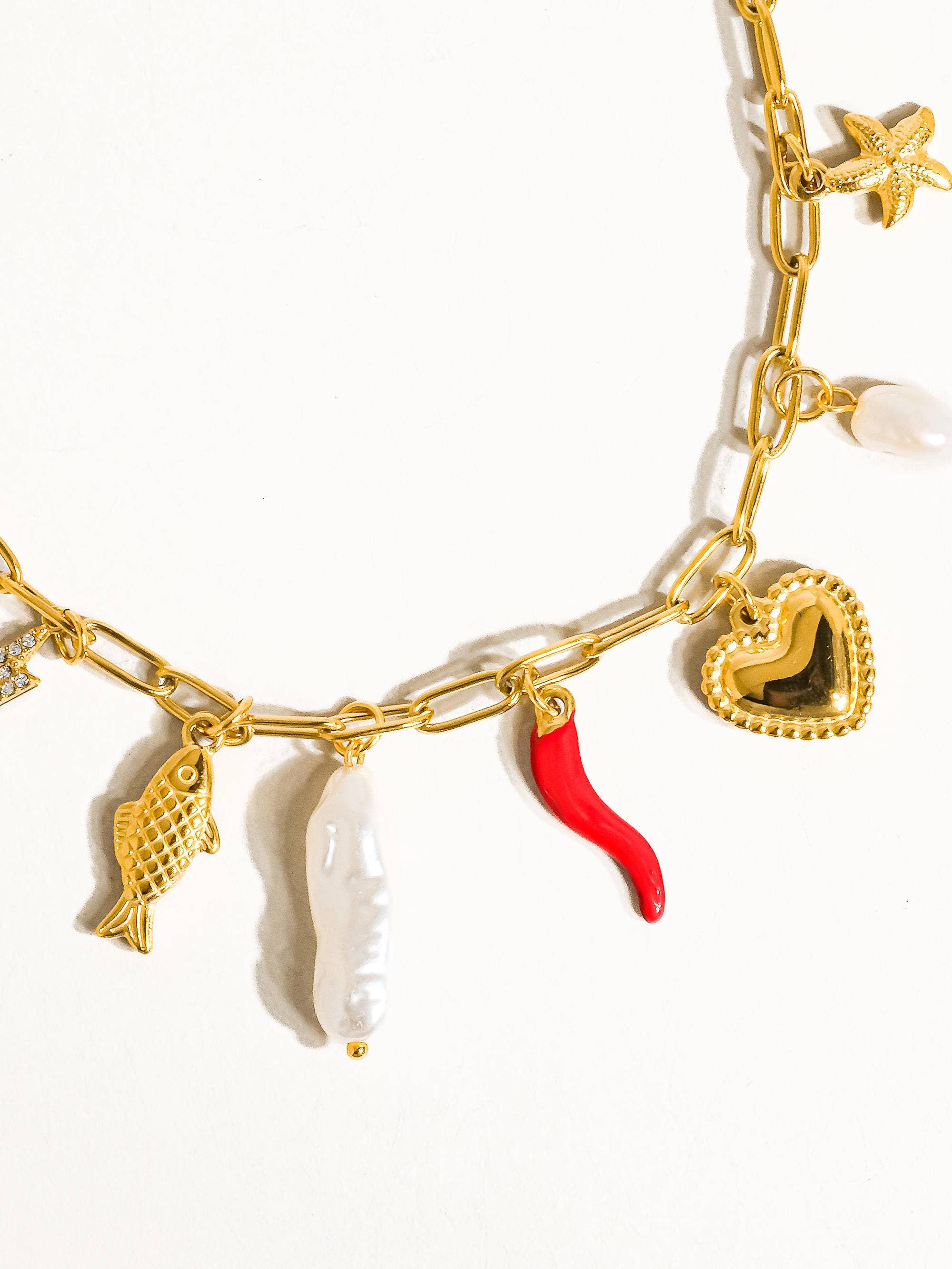 Gold necklace with various charms including a red chili pepper, fish, and heart on a white background
