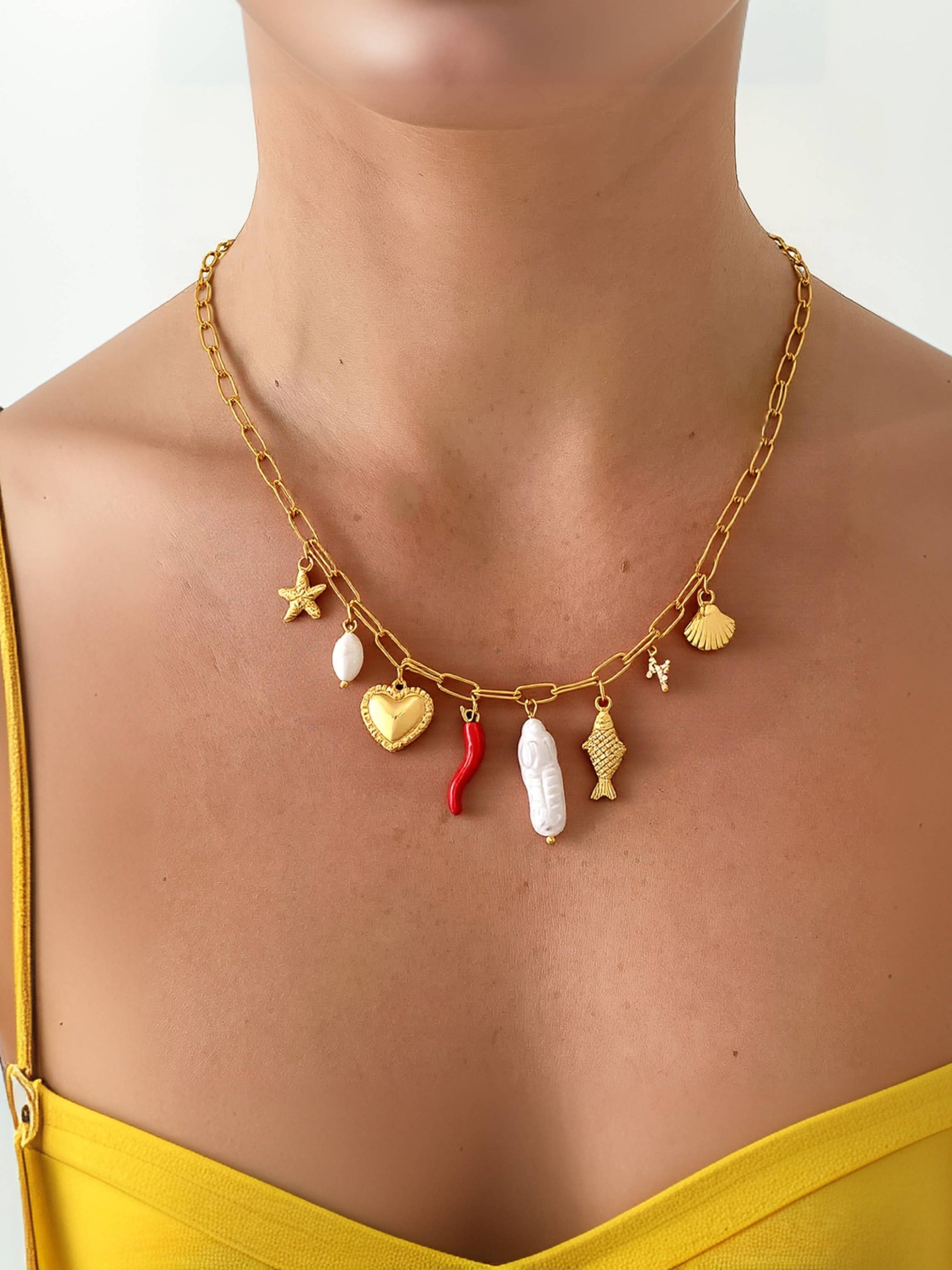 Gold necklace with various charms on a person wearing a yellow top.