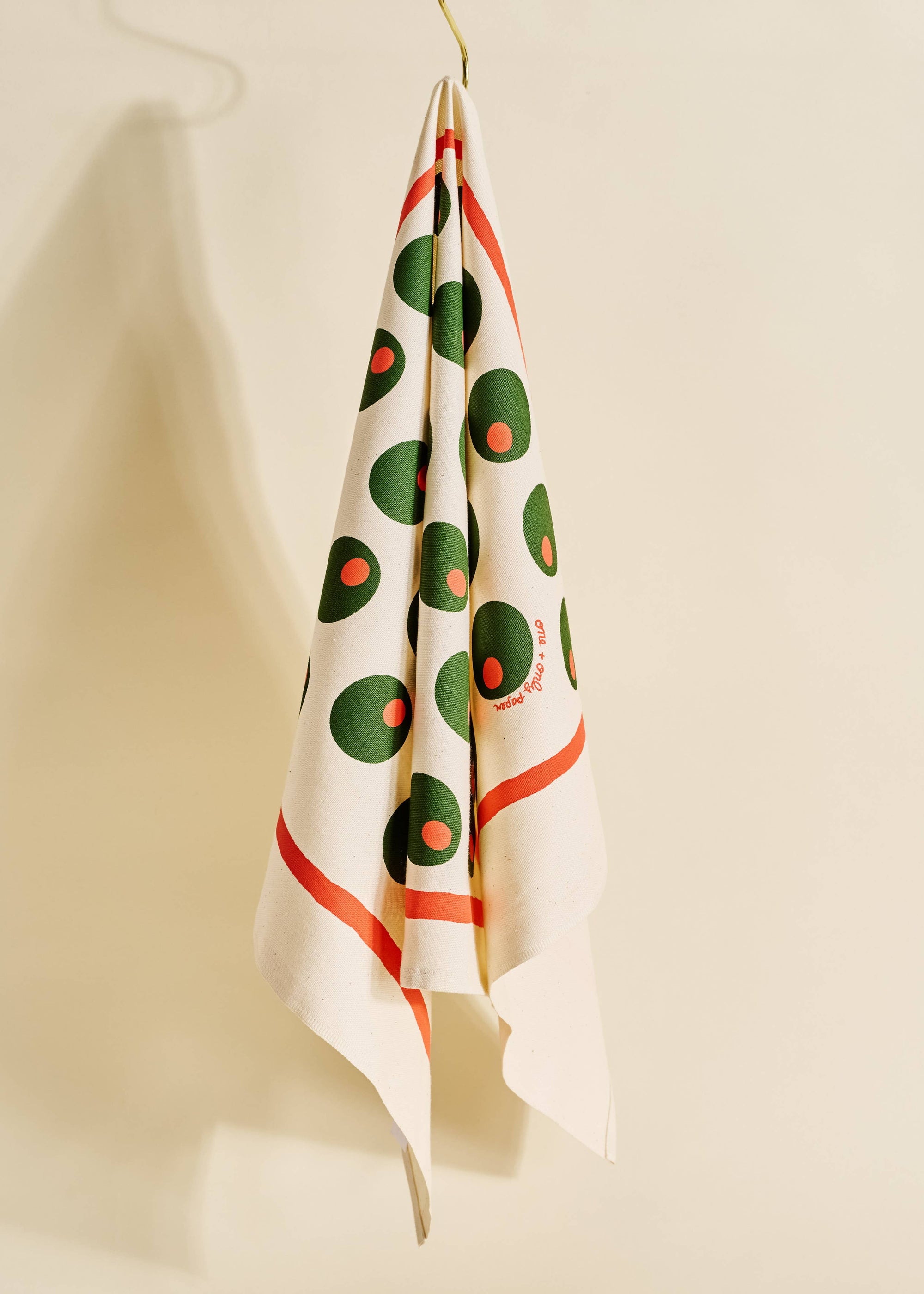 Decorative towel with green and red pattern hanging on a hook against a beige wall.