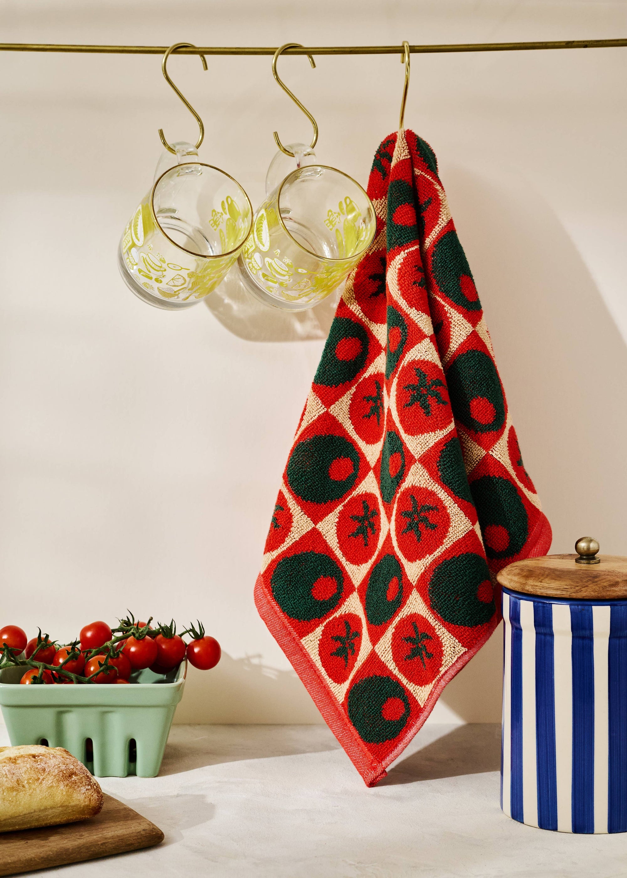 Red and black patterned towel hanging on a hook with a container and tomatoes in the background.