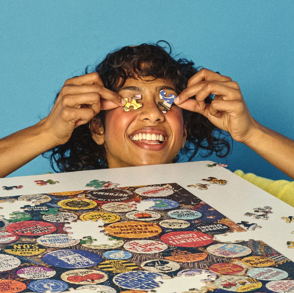 Person with colorful stickers on their eyes, sitting at a table with a puzzle featuring bottle caps.
