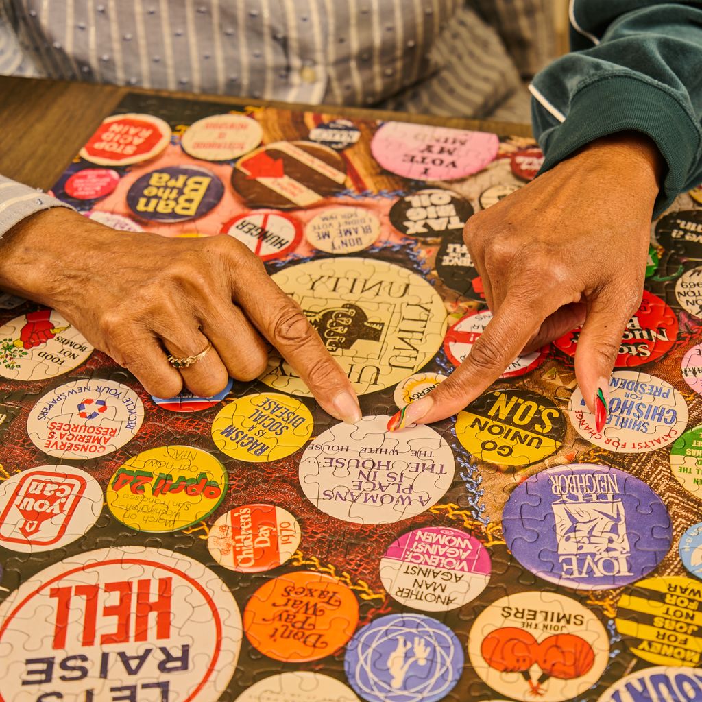 Close-up of a table covered with various colorful buttons, with hands interacting with them.