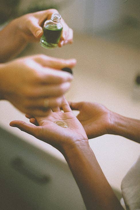 Person applying a green liquid from a small bottle onto another person's palm.